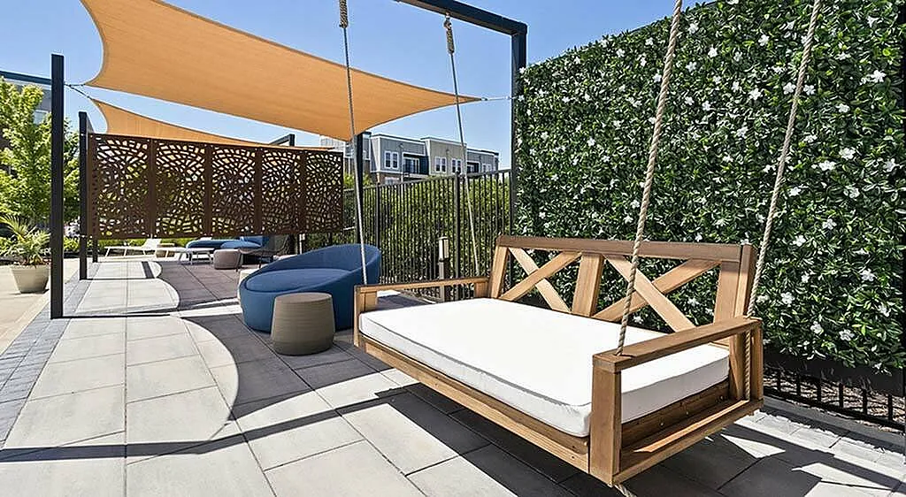 Modern outdoor patio featuring a stylish wooden swing, elegant shade sails, and vibrant greenery for a relaxing vibe.