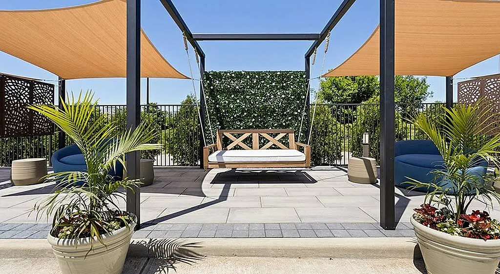 Luxurious outdoor patio with modern swing, vibrant greenery, and stylish sun shades, perfect for relaxation.