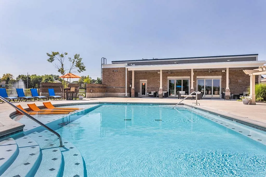 Inviting outdoor pool area with modern loungers and umbrellas, set against a stylish clubhouse, perfect for relaxation and leisure.