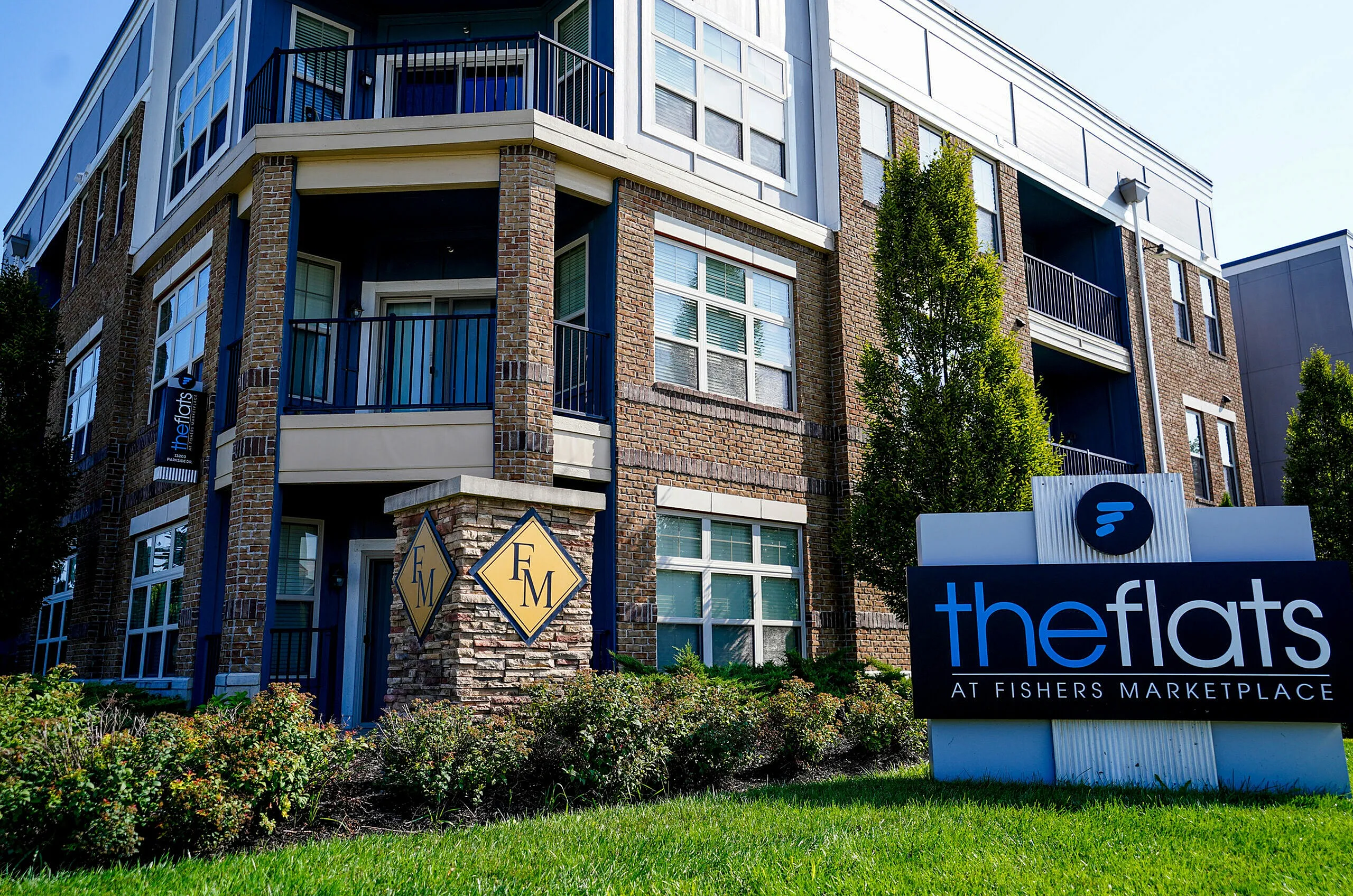 Modern apartment complex exterior with elegant brickwork and lush landscaping at The Flats at Fishers Marketplace.