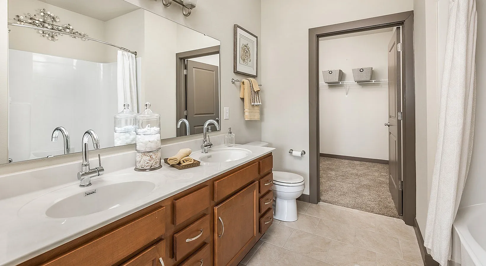 Modern bathroom with dual sinks, elegant wooden cabinetry, and a spacious walk-in closet showcasing a serene and functional space.