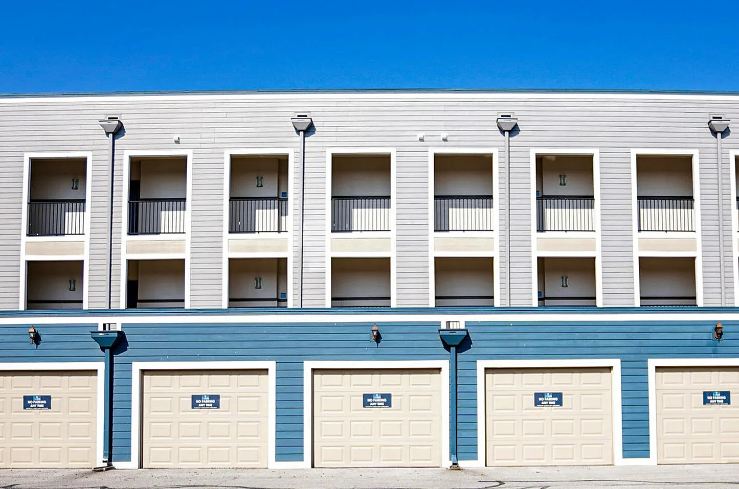 Modern apartment complex with a sleek design, featuring multiple balconies and ground-level garages under a clear blue sky.