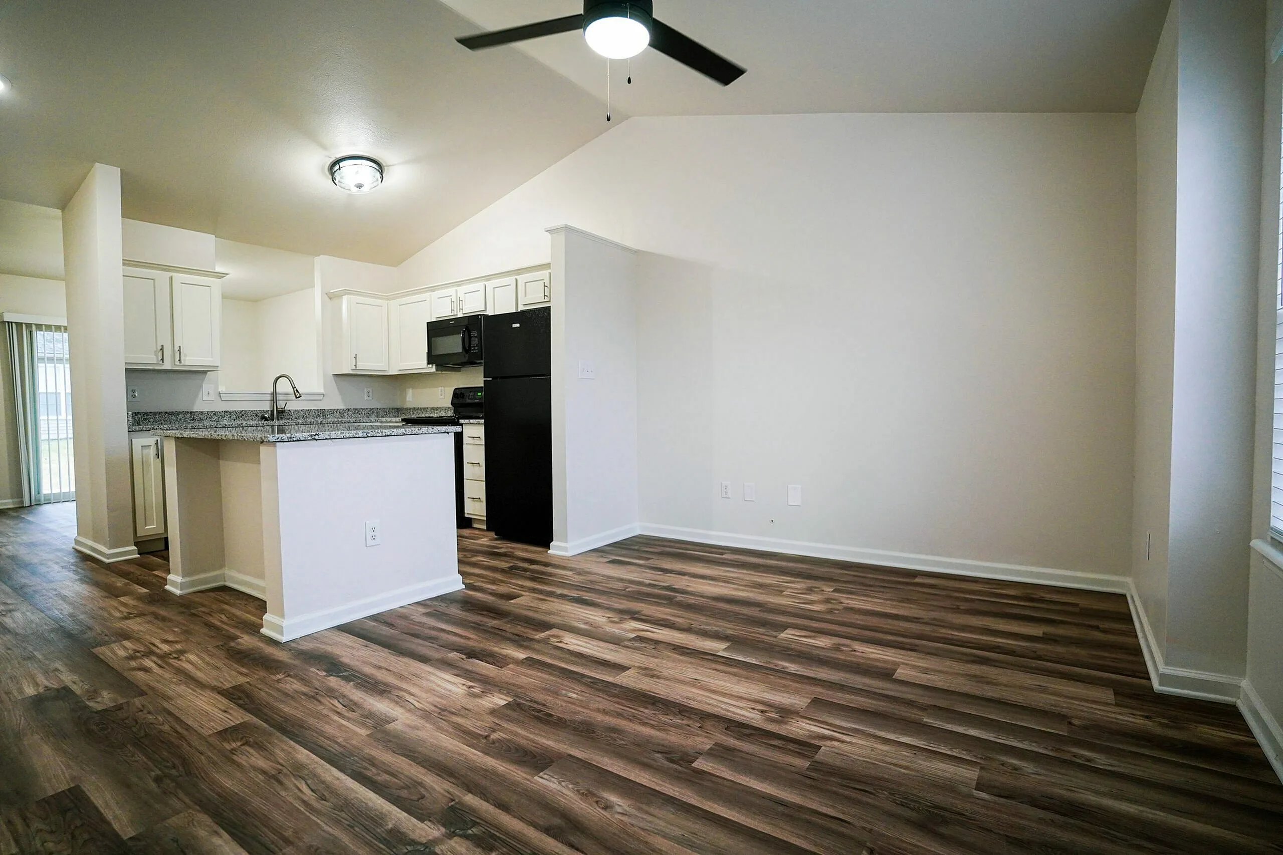Modern open-plan kitchen and living area with elegant wooden flooring, sleek white cabinetry, and a central island under stylish lighting.