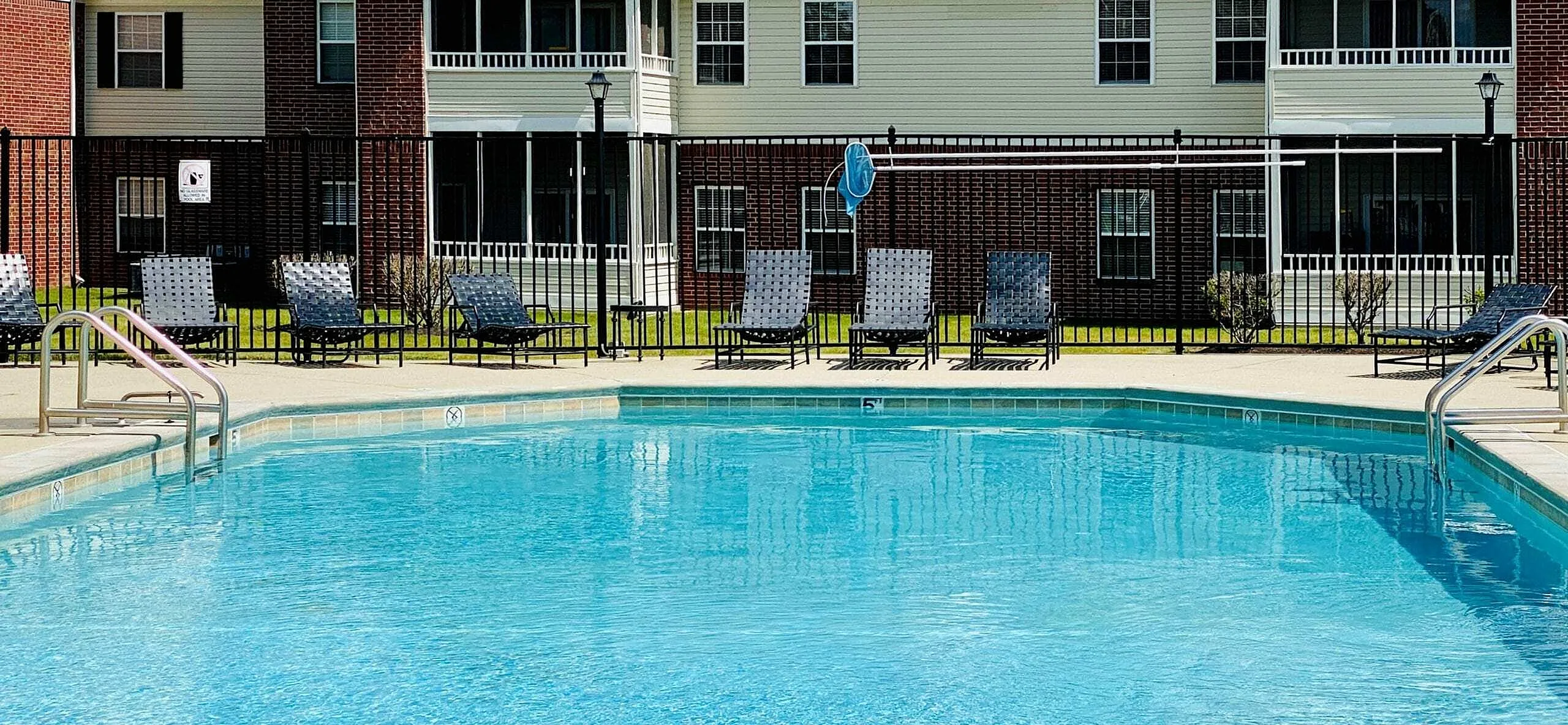 Inviting apartment complex with a sparkling swimming pool and comfortable lounge chairs, perfect for relaxation.