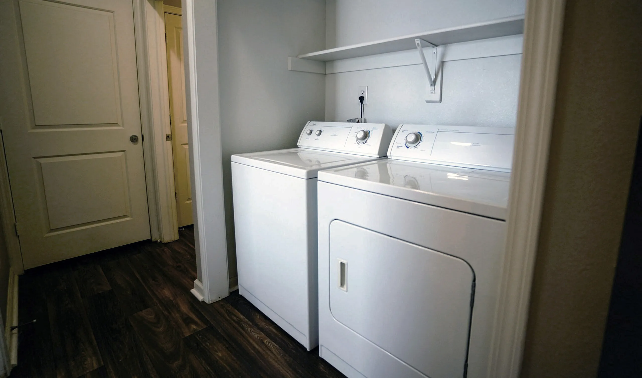 Elegant laundry nook with modern washer and dryer, complemented by sleek dark wood flooring.