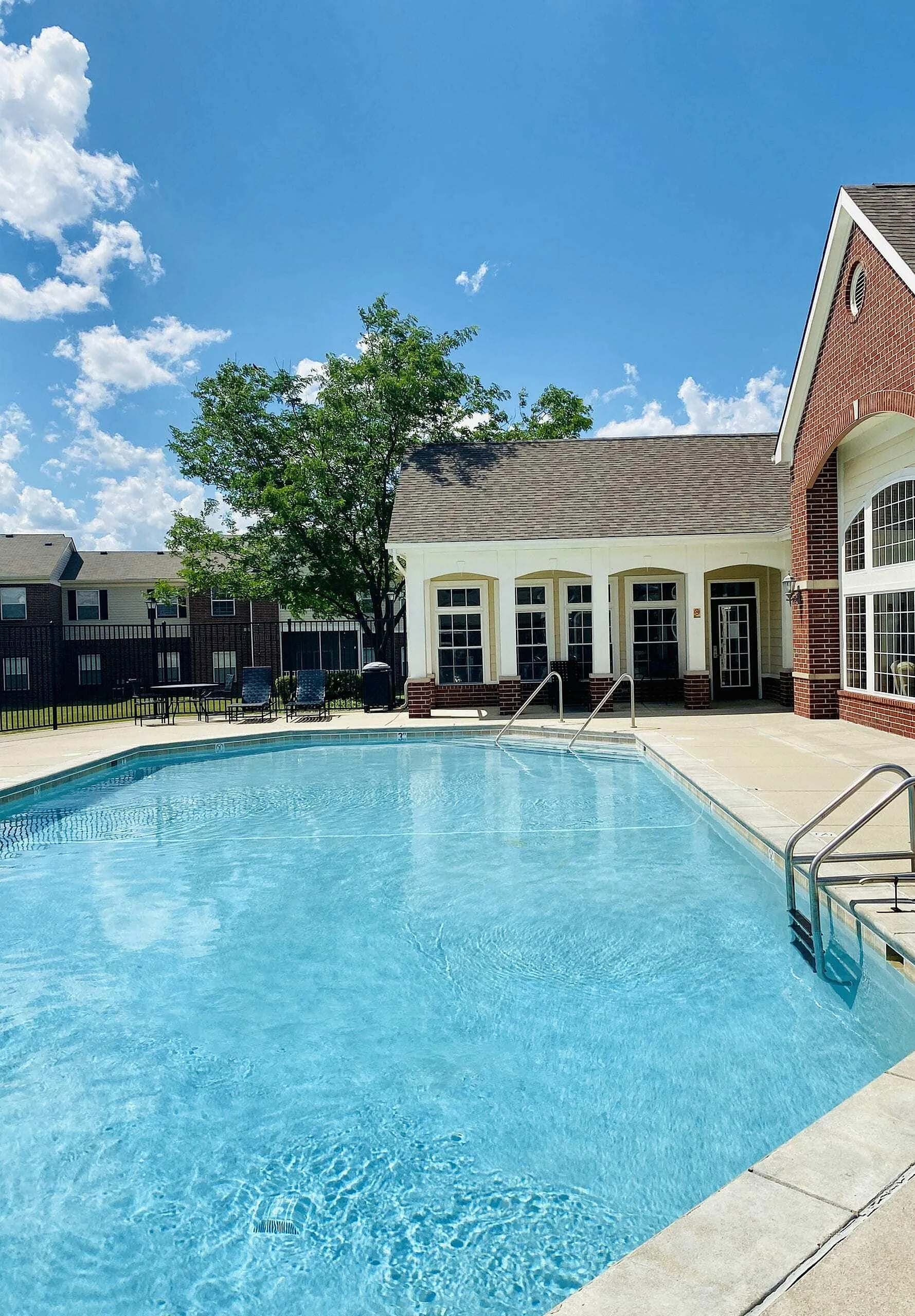 Inviting outdoor pool in a sunny residential setting with elegant brick architecture and lush greenery.