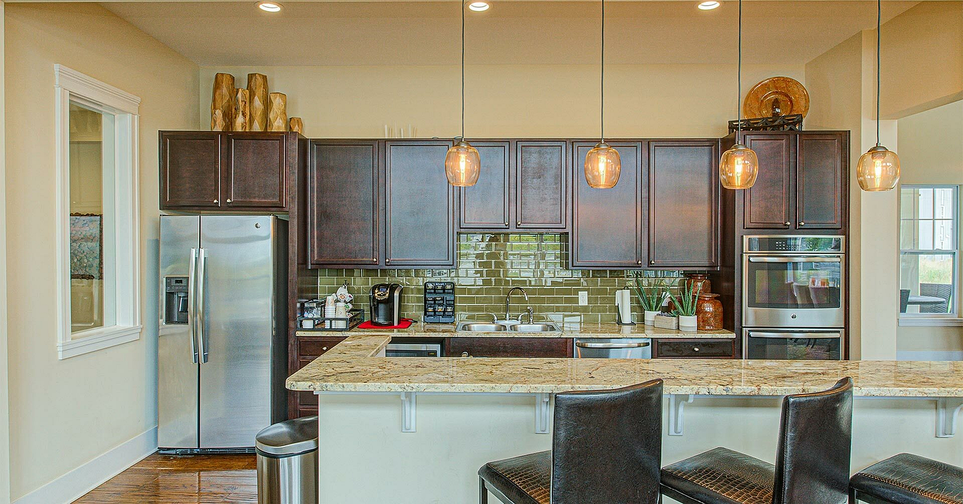 Elegant kitchen featuring dark wood cabinets, stainless steel appliances, modern pendant lighting, and a sleek granite countertop bar area perfect for entertaining.
