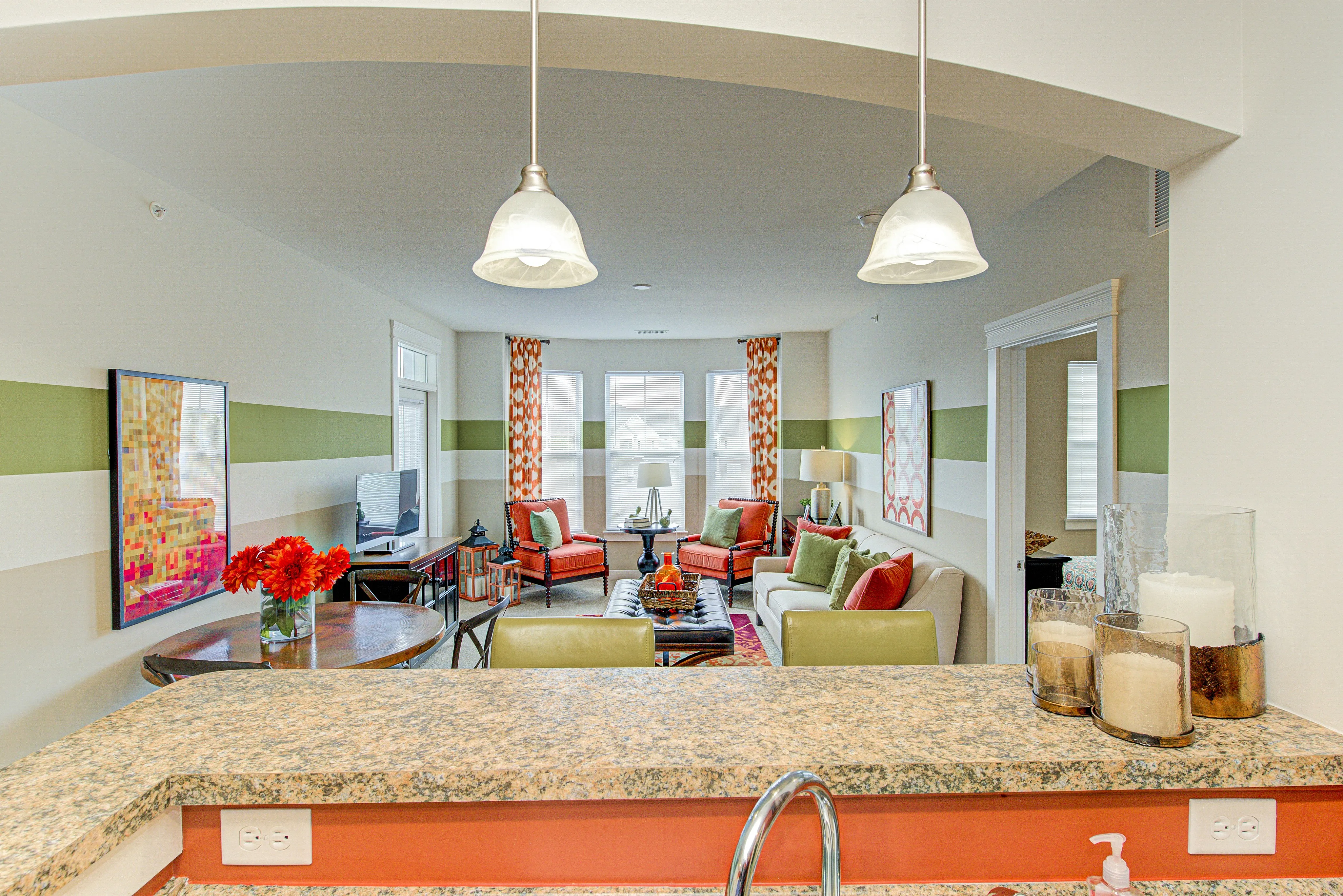 Bright and inviting living room with modern decor, vibrant seating, and plentiful natural light, viewed from a stylish kitchen countertop.