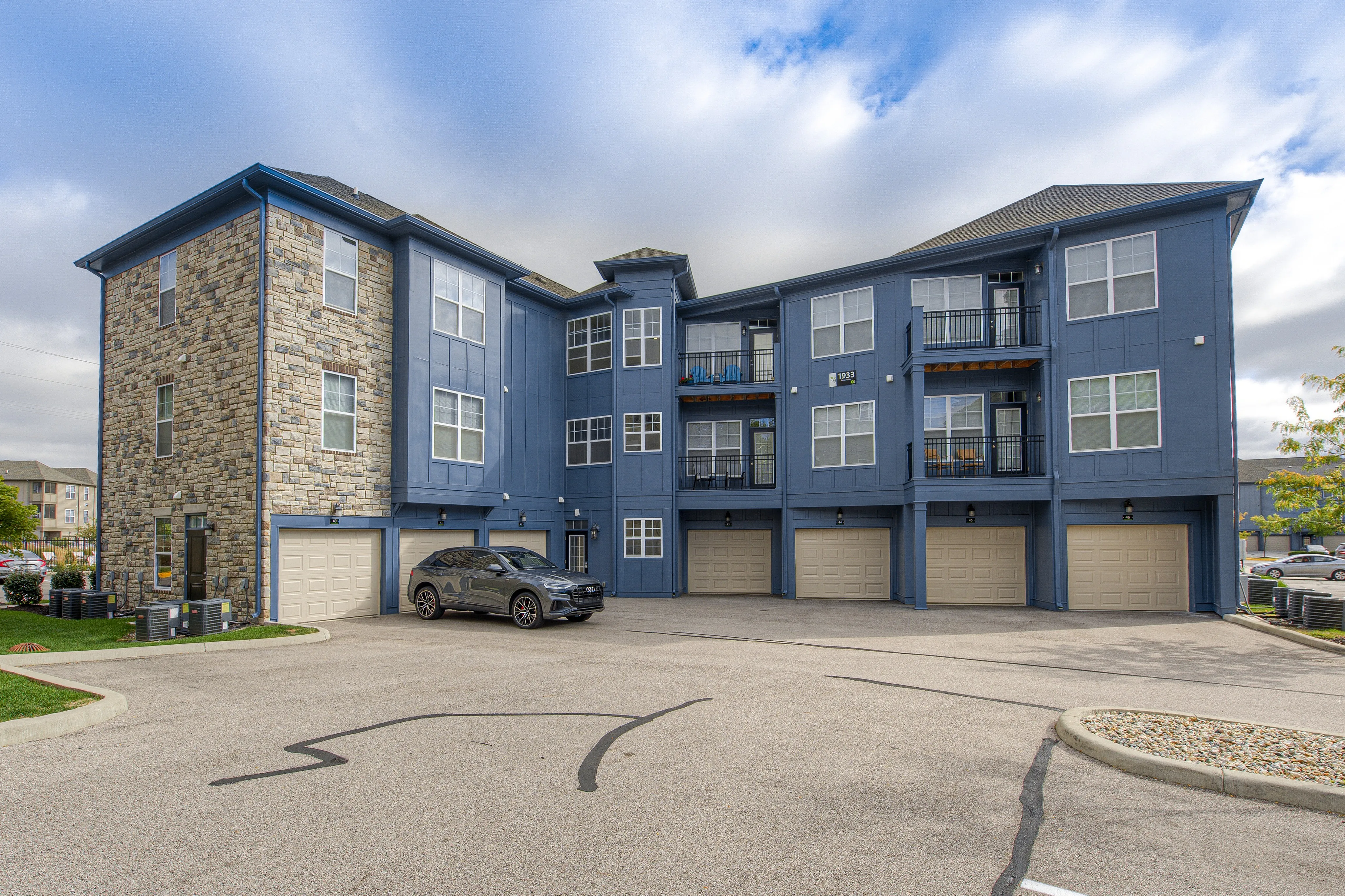 Modern apartment building with elegant stone facade and convenient garage access, surrounded by a clean and spacious parking area.