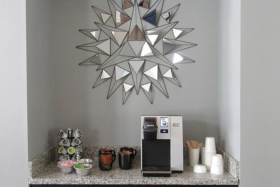 Modern coffee station with sleek Keurig machine, stylish geometric mirror, and ample countertop space, perfect for a refreshing break.