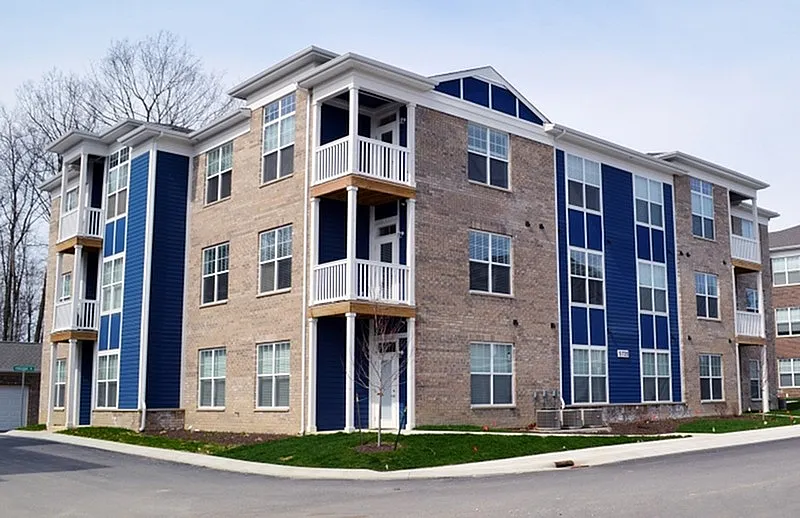 Modern three-story apartment building with stylish brick and blue-panel exterior, surrounded by a serene suburban neighborhood.
