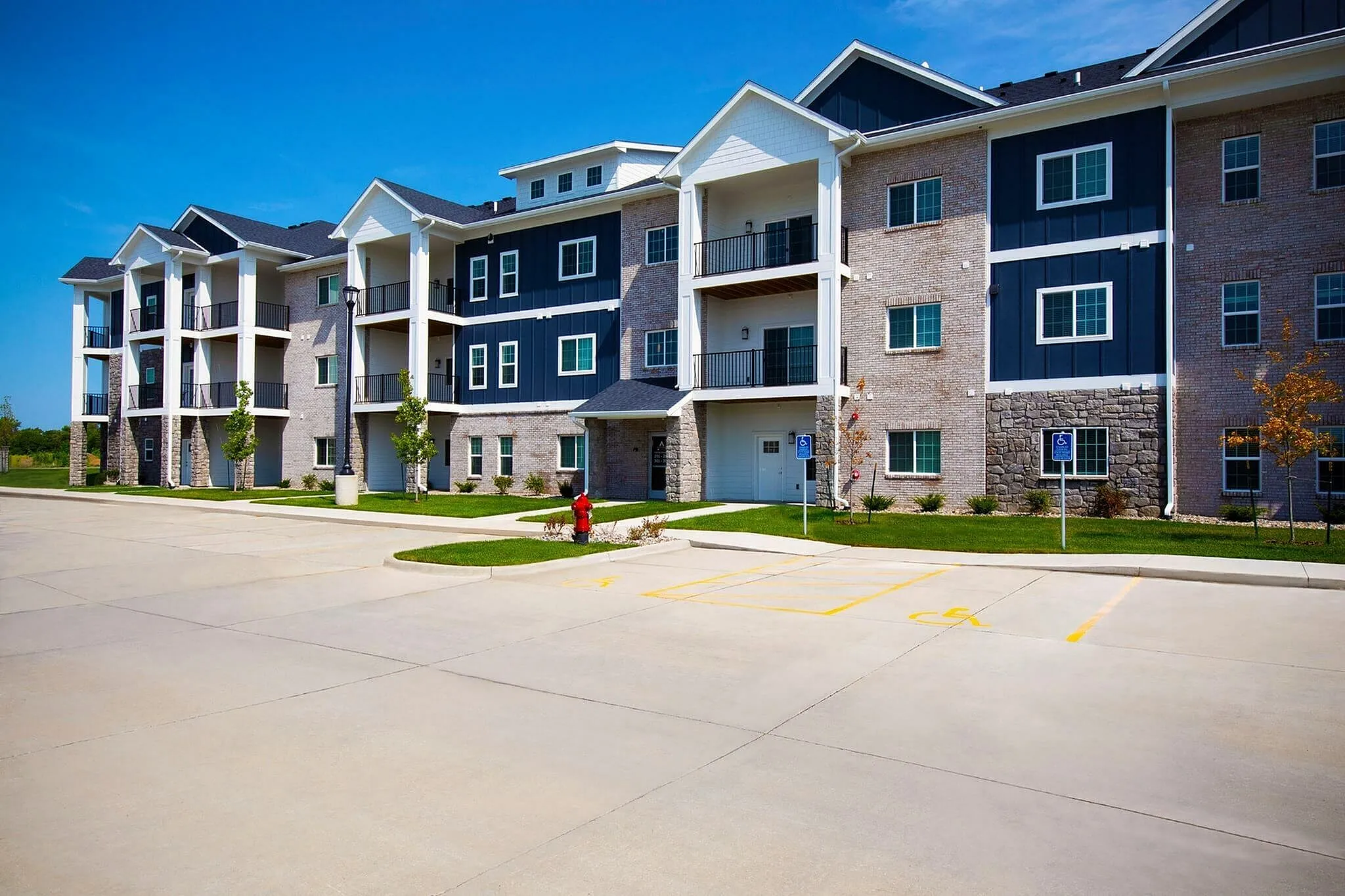 Charming three-story apartment building with modern balconies, surrounded by green lawns under a clear blue sky.