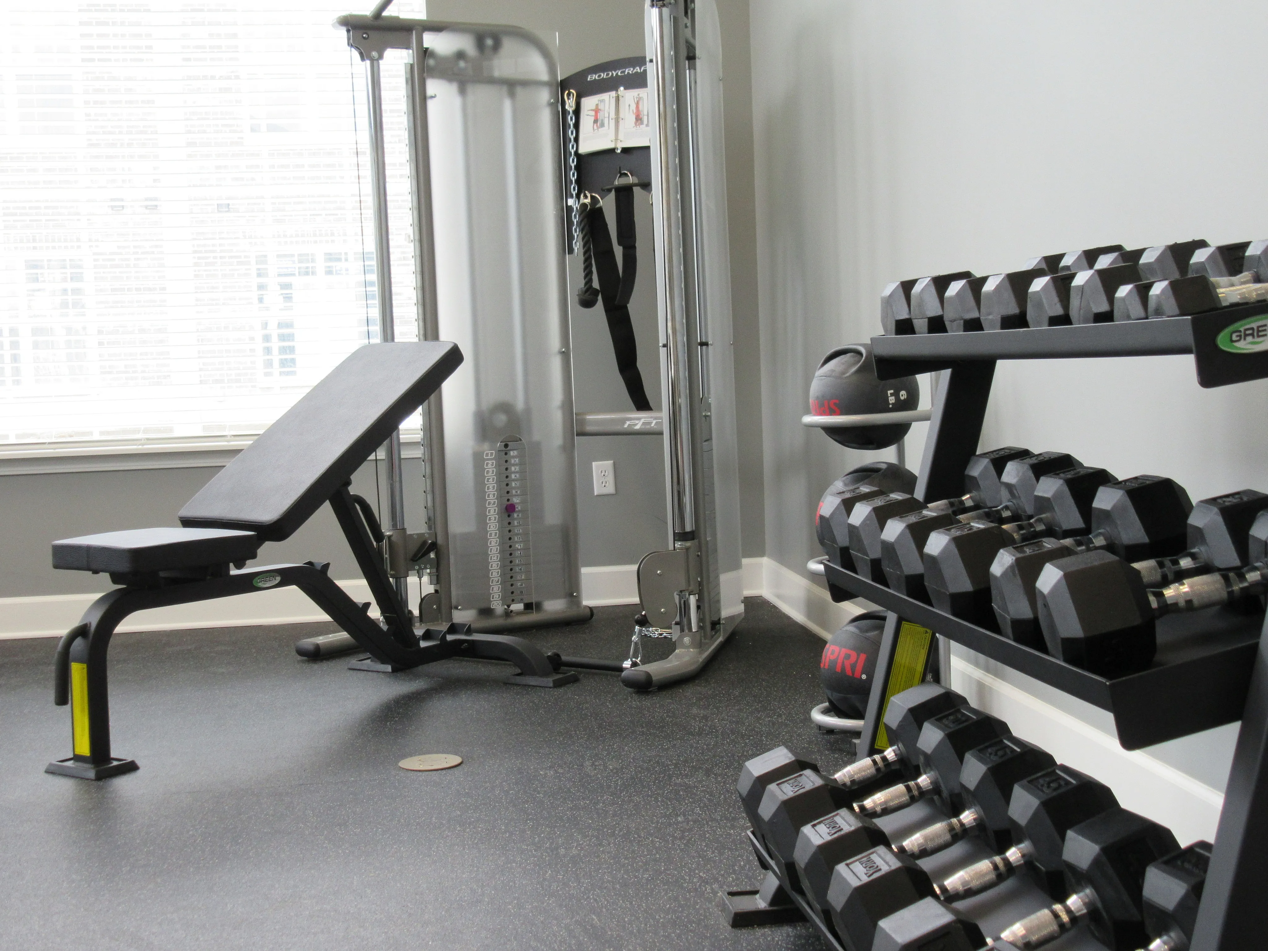 Modern home gym with weight bench, multi-gym equipment, and a neatly organized rack of dumbbells.