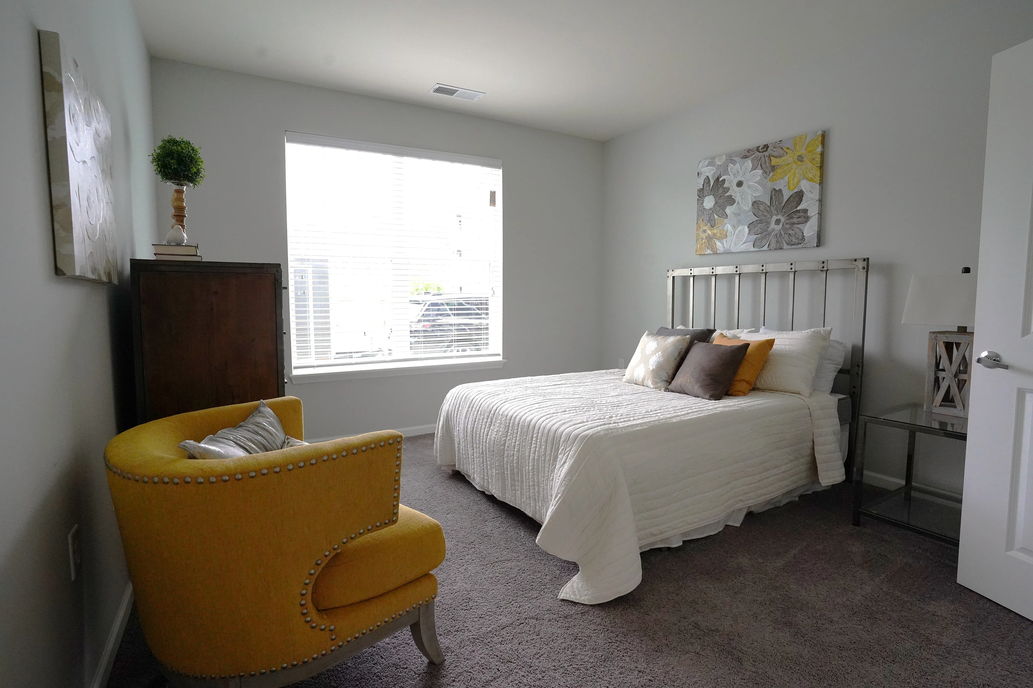 Cozy bedroom with elegant decor, featuring a plush bed with decorative pillows, a vibrant yellow armchair, and large windows for ample natural light.