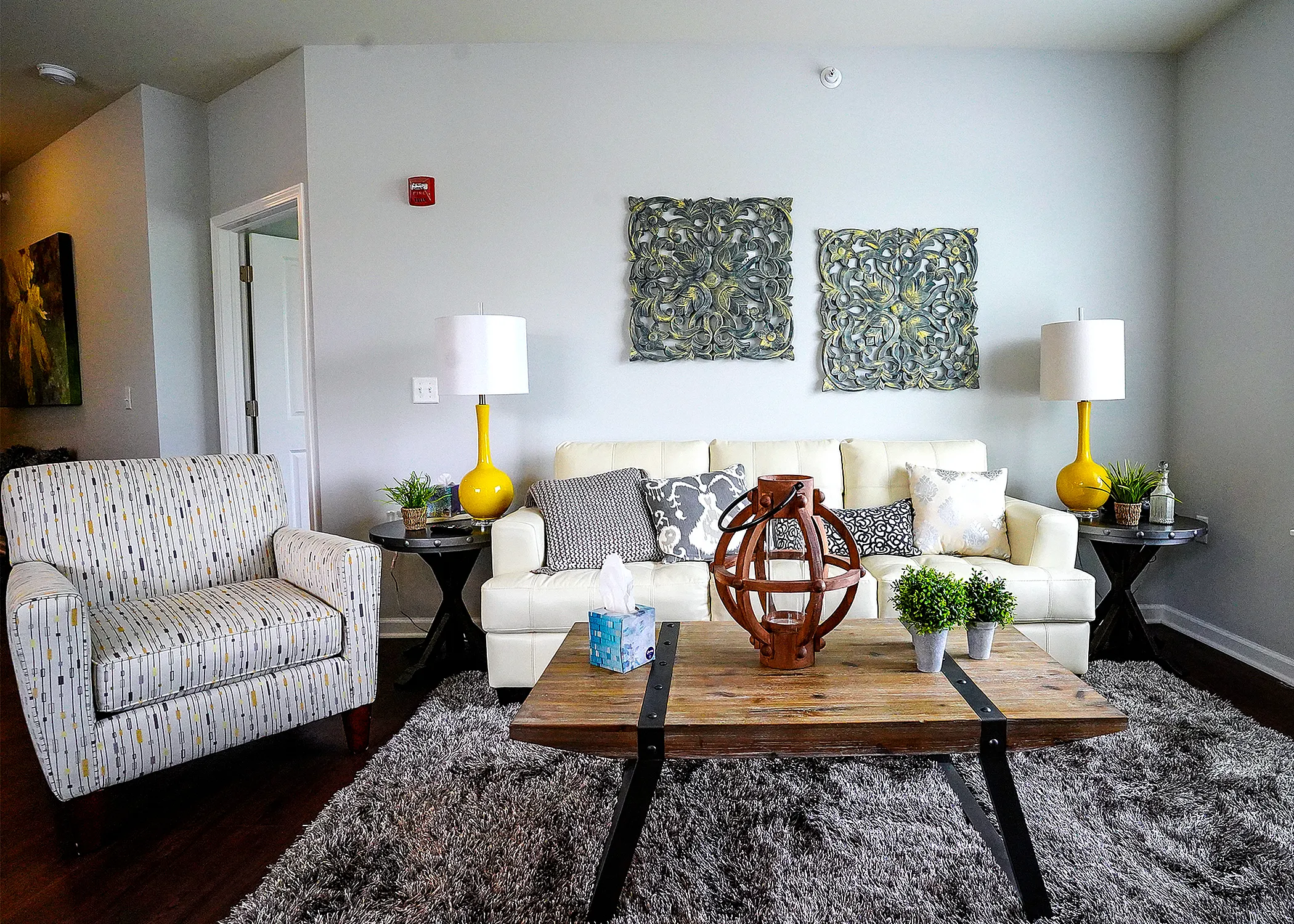 Chic living room with a cozy white sofa, stylish armchair, and elegant coffee table on a plush rug, accented by vibrant yellow lamps and artistic wall decor.