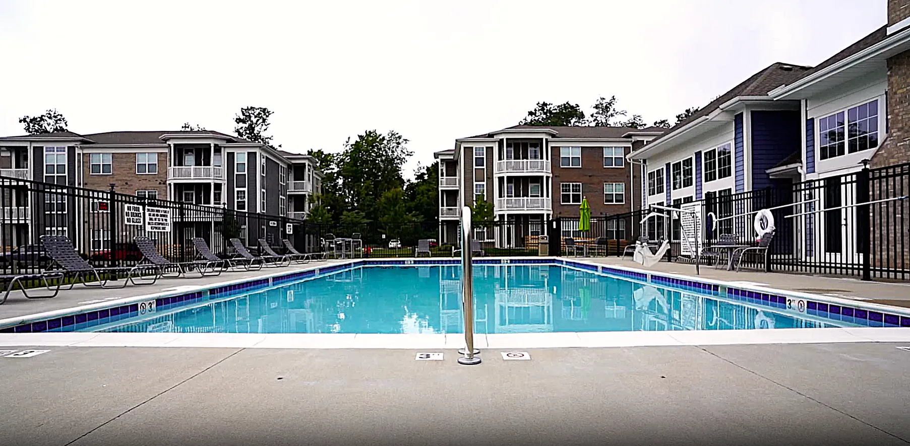 Luxurious apartment complex with a sparkling outdoor pool, surrounded by elegant multi-story buildings and lush greenery.