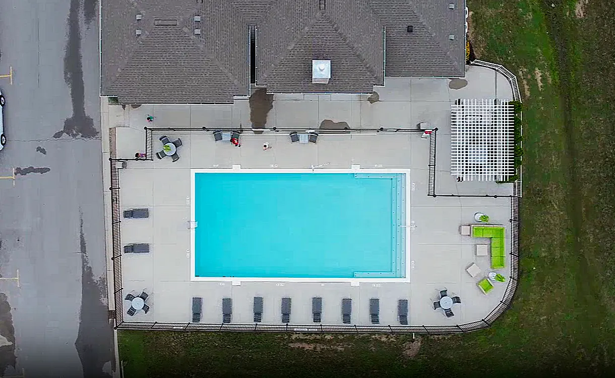 Aerial view of a modern apartment complex with a pristine swimming pool, surrounded by comfortable lounge chairs and green seating areas, inviting relaxation and enjoyment.