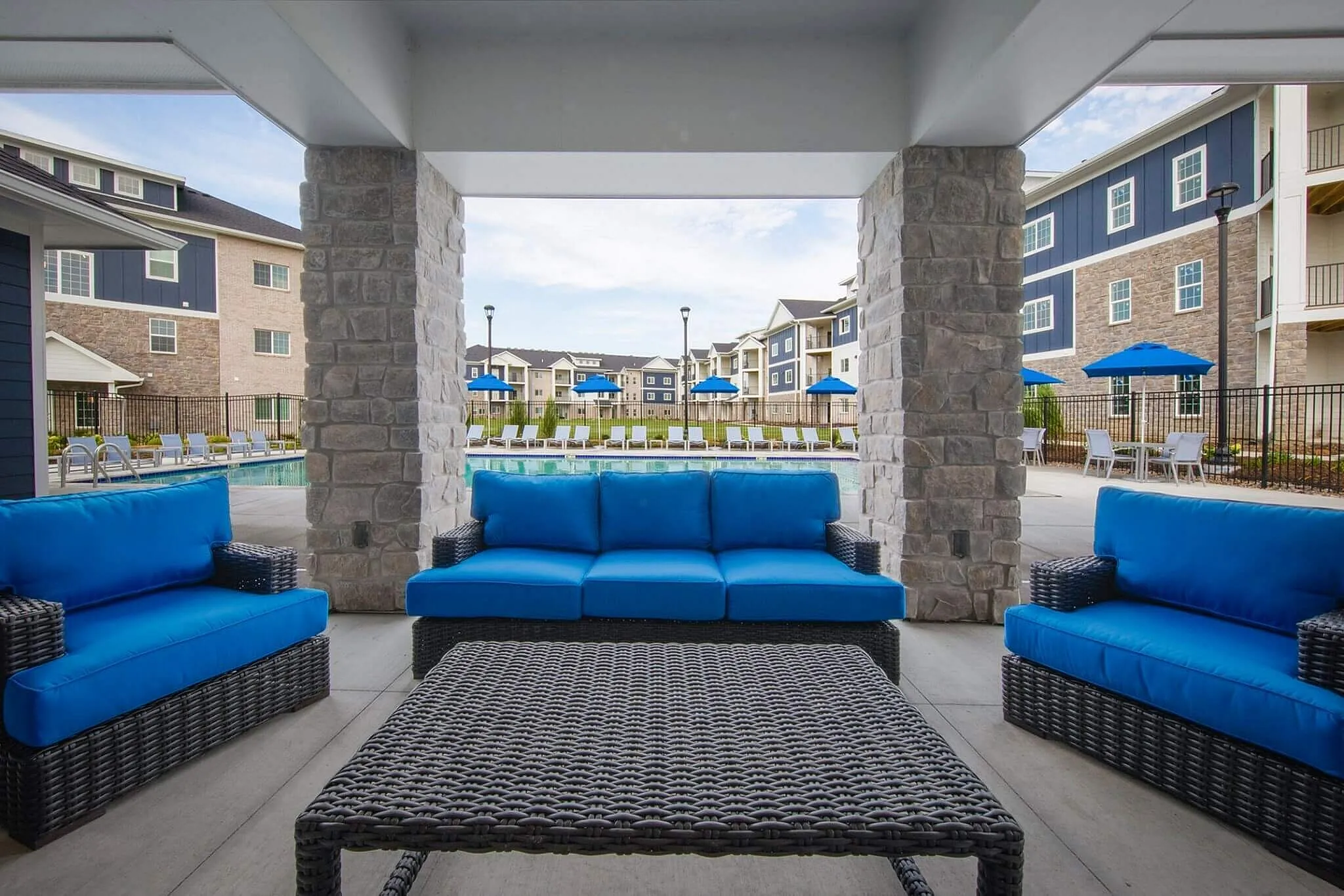 Chic outdoor lounge area with vibrant blue seating overlooking a sparkling pool and modern apartment complex.