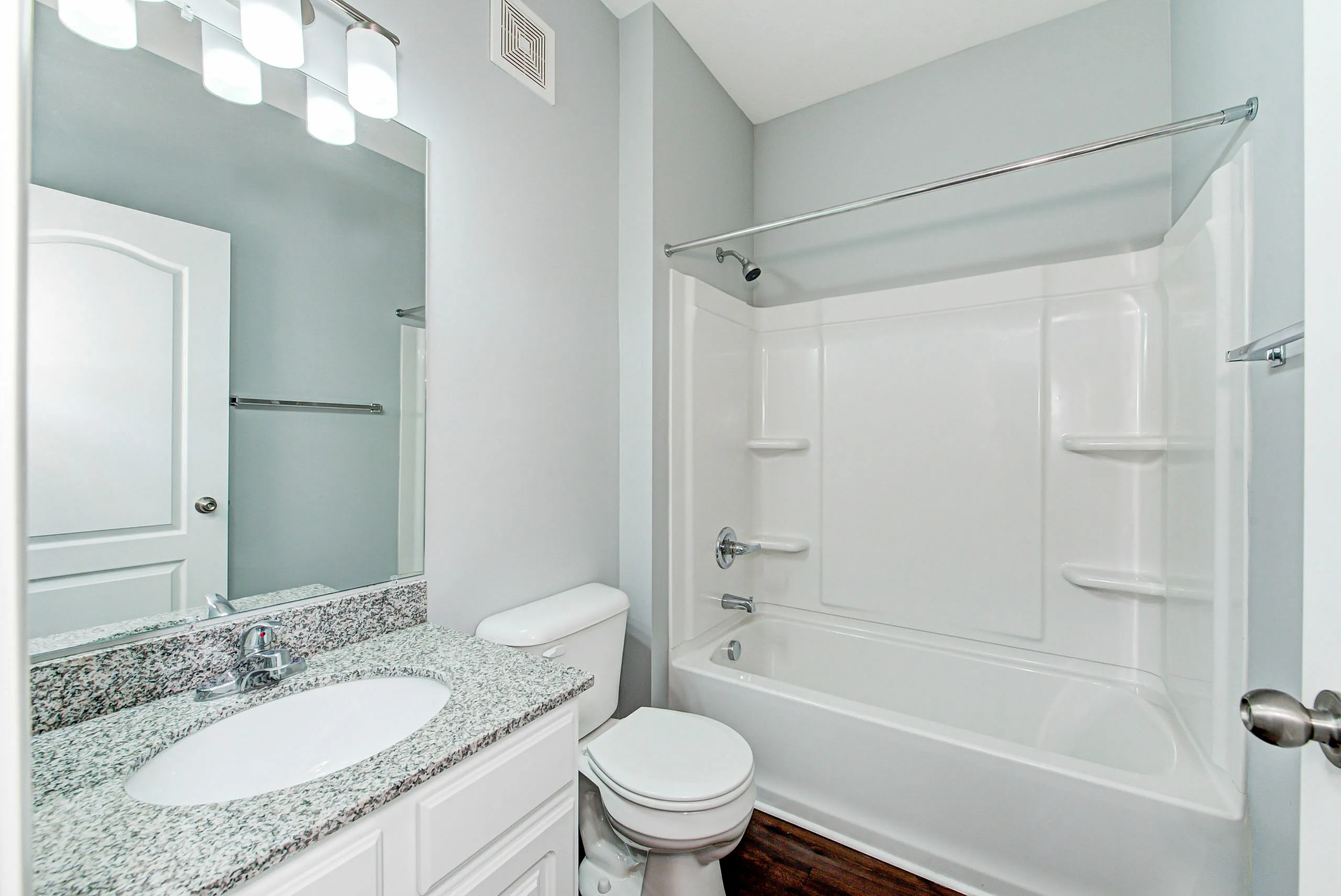 Modern bathroom featuring a sleek granite countertop, elegant lighting, and a pristine white bathtub.