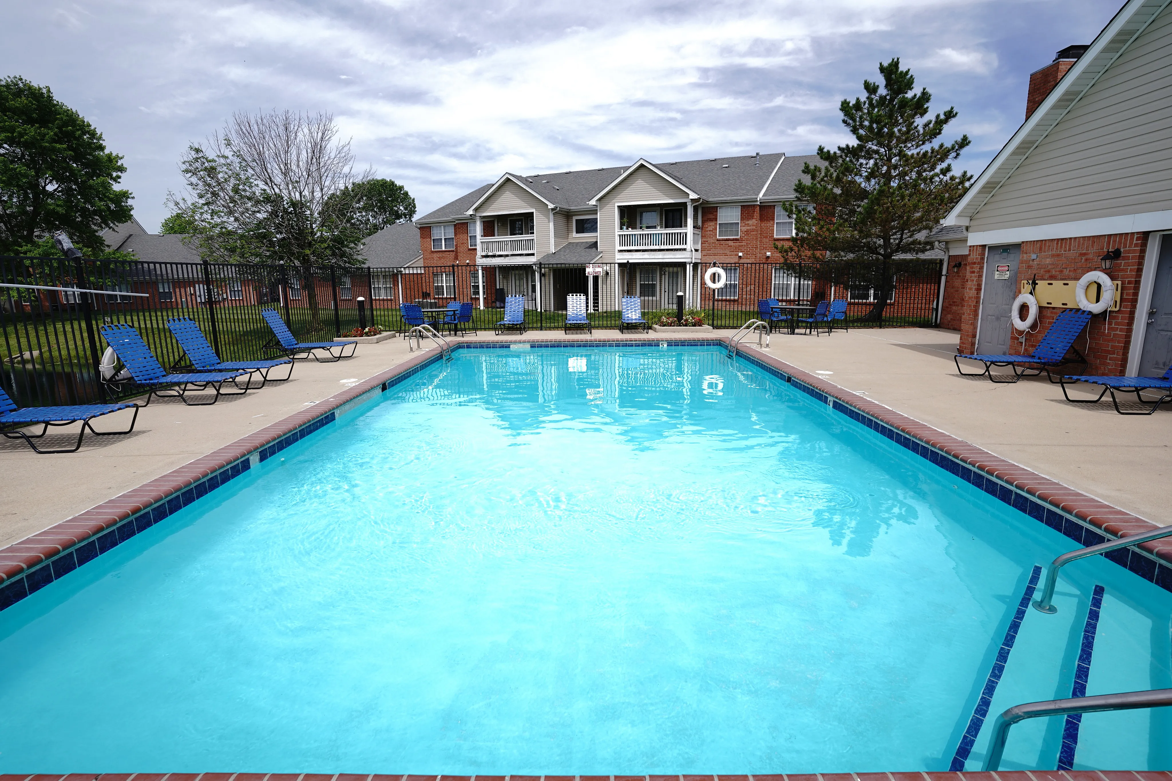 Inviting apartment complex with a sparkling swimming pool, surrounded by comfortable lounge chairs and lush green landscaping.