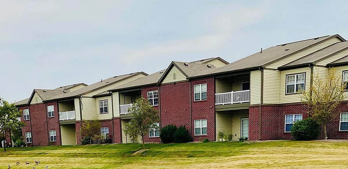Charming apartment complex with red brick facade, featuring spacious balconies and surrounded by lush greenery and well-maintained lawns.
