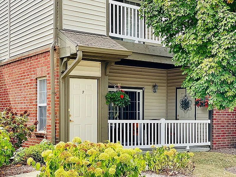 Charming apartment exterior with a cozy private porch, lush greenery, and vibrant flowers.