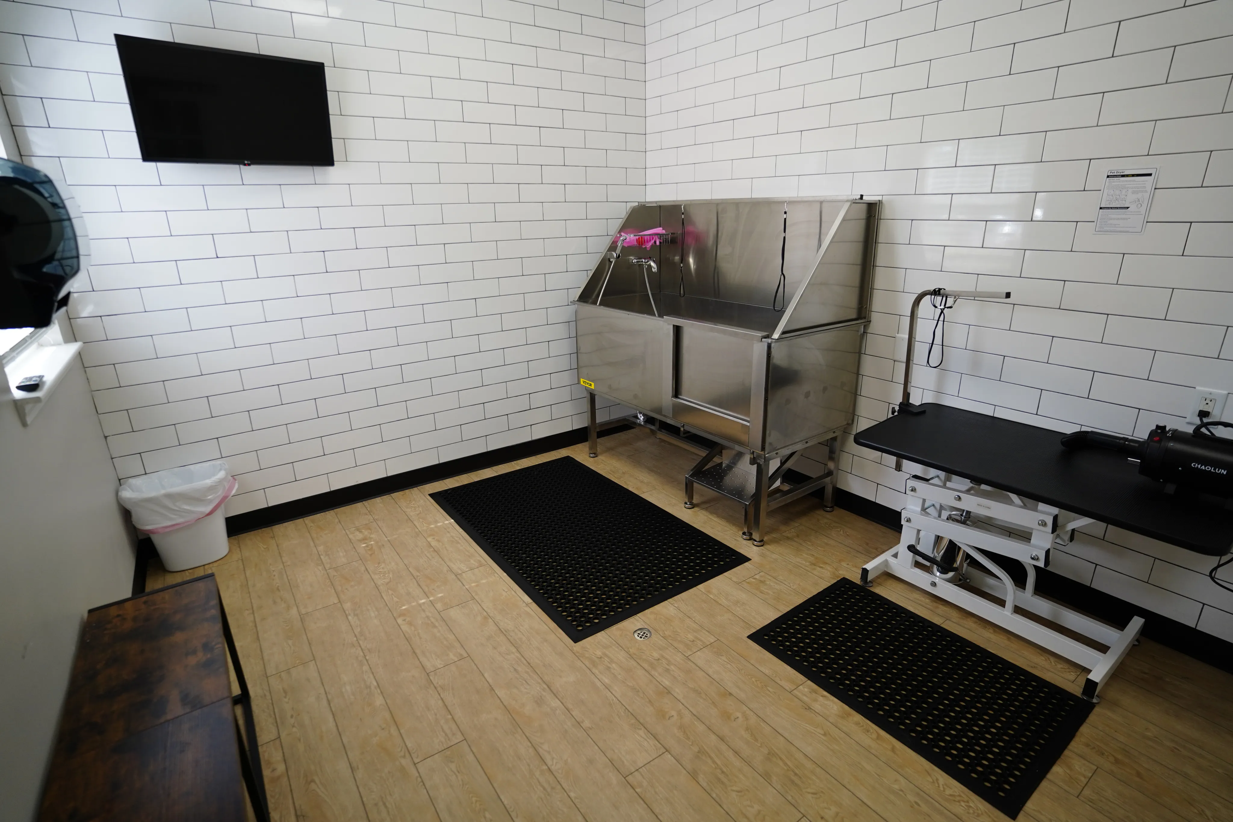 Modern grooming station with sleek stainless steel tub, tiled walls, and flat-screen TV, providing a clean and professional environment.