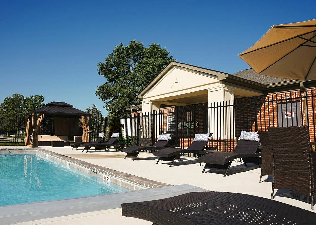 Inviting outdoor pool area with elegant lounge chairs, a shaded cabana, and a charming clubhouse under a clear blue sky.