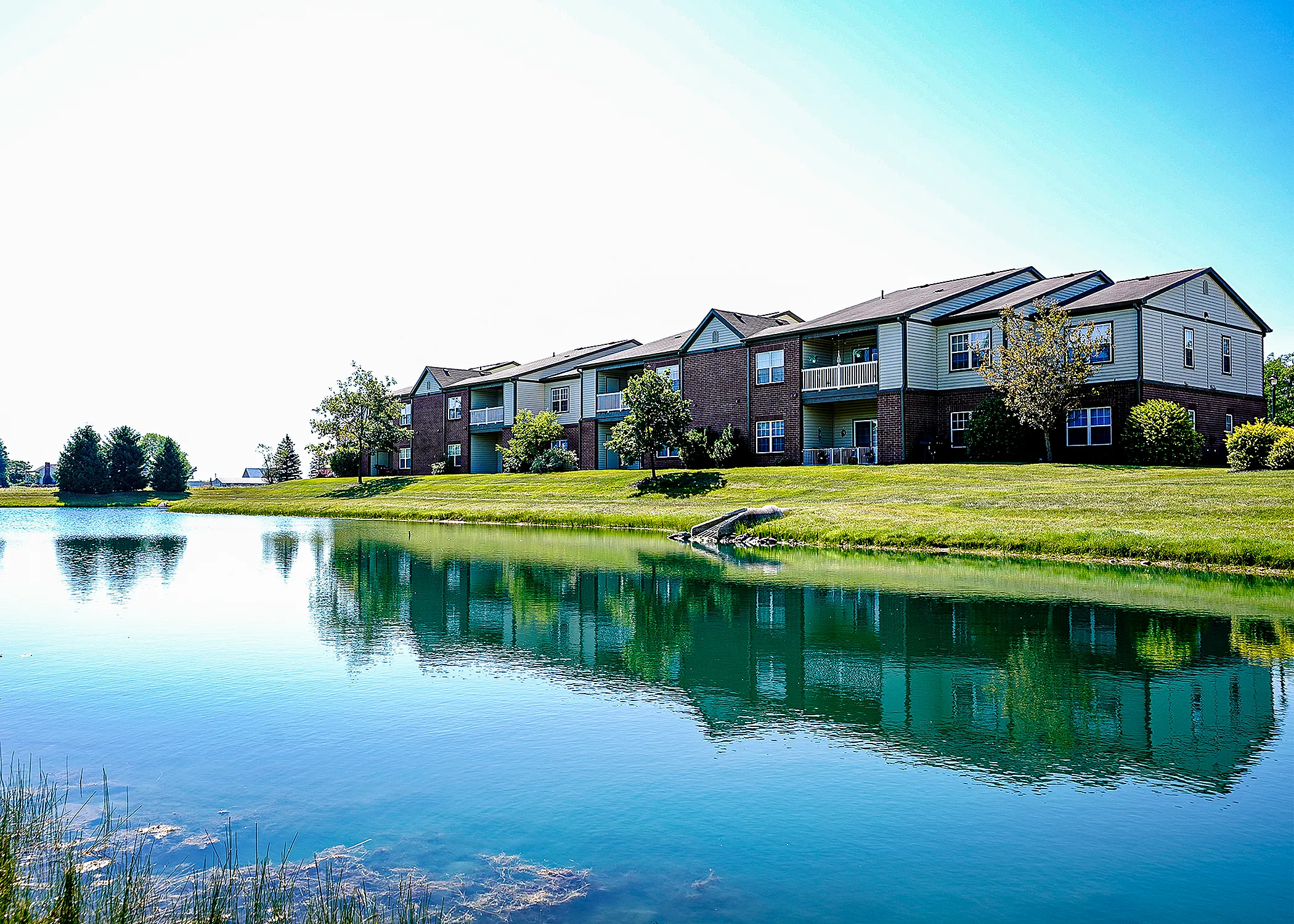 Luxury apartments overlooking a serene pond with lush green surroundings and pristine architecture.