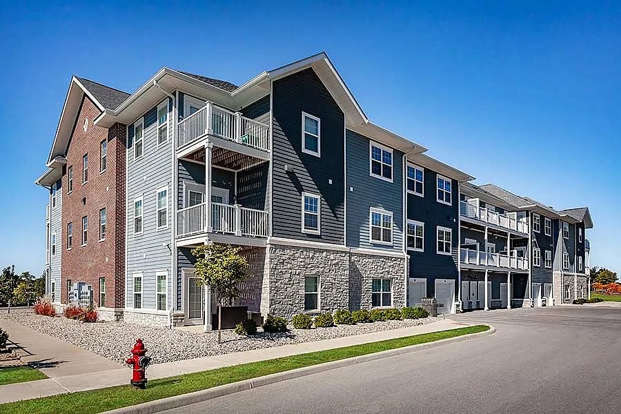 Charming modern apartment building with a blend of brick and siding, featuring balconies and lush landscaping in a peaceful neighborhood.
