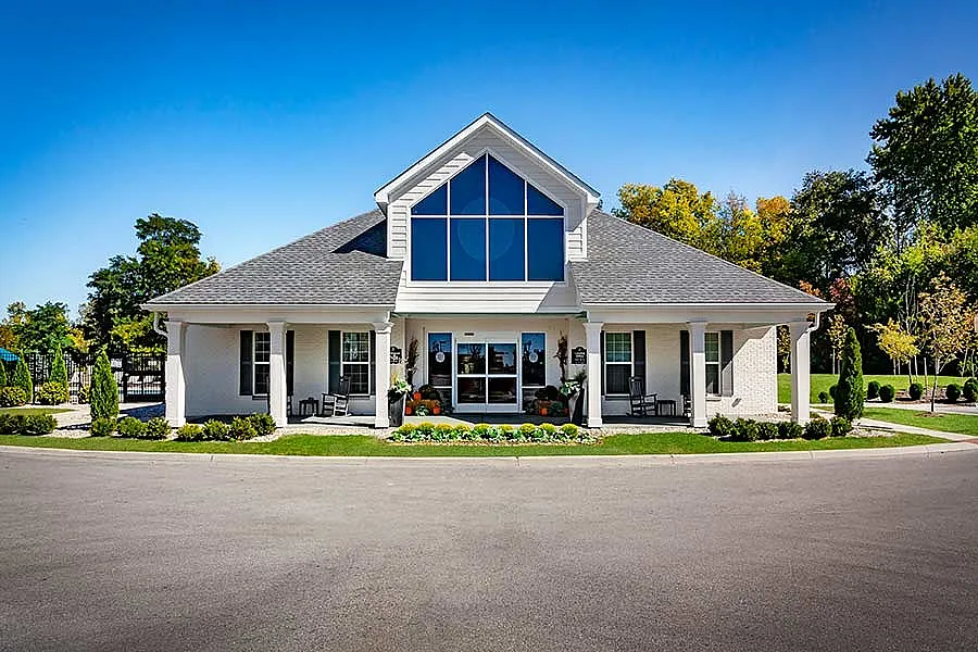 Charming suburban house with a symmetrical design, featuring a gabled roof and large central windows, surrounded by lush greenery and a manicured lawn.