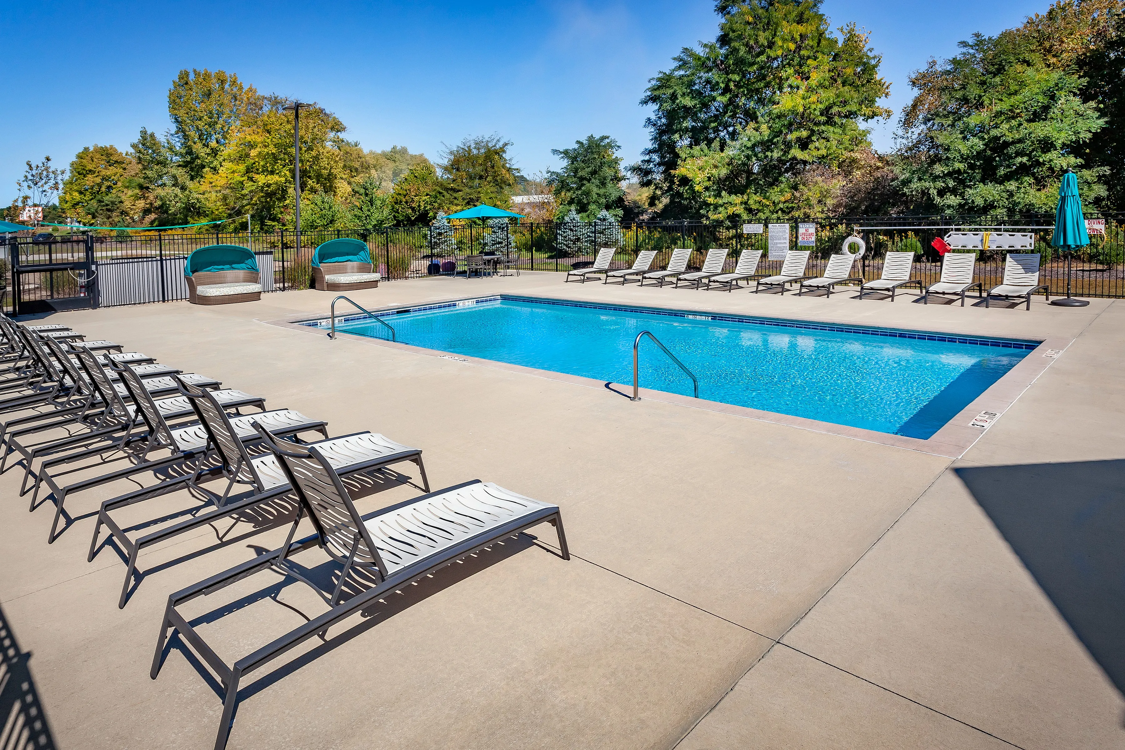 Inviting outdoor pool area with sleek lounge chairs, surrounded by lush greenery and vibrant blue skies.