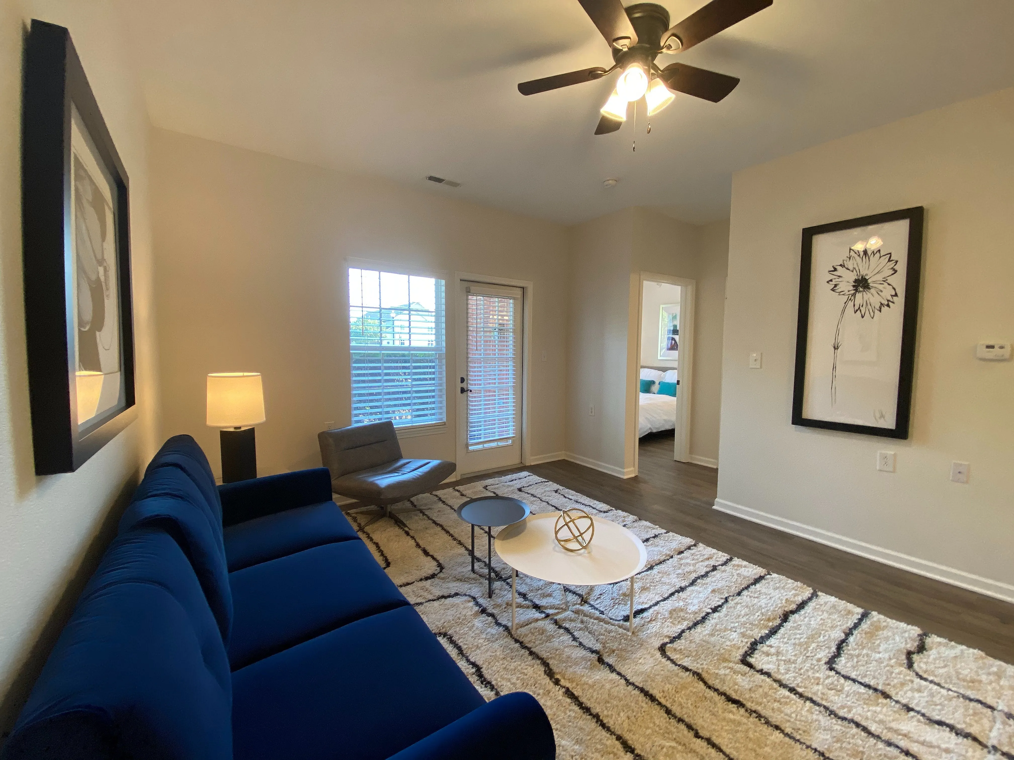 Chic living room with a plush blue sofa, elegant artwork, and natural light streaming through large windows.