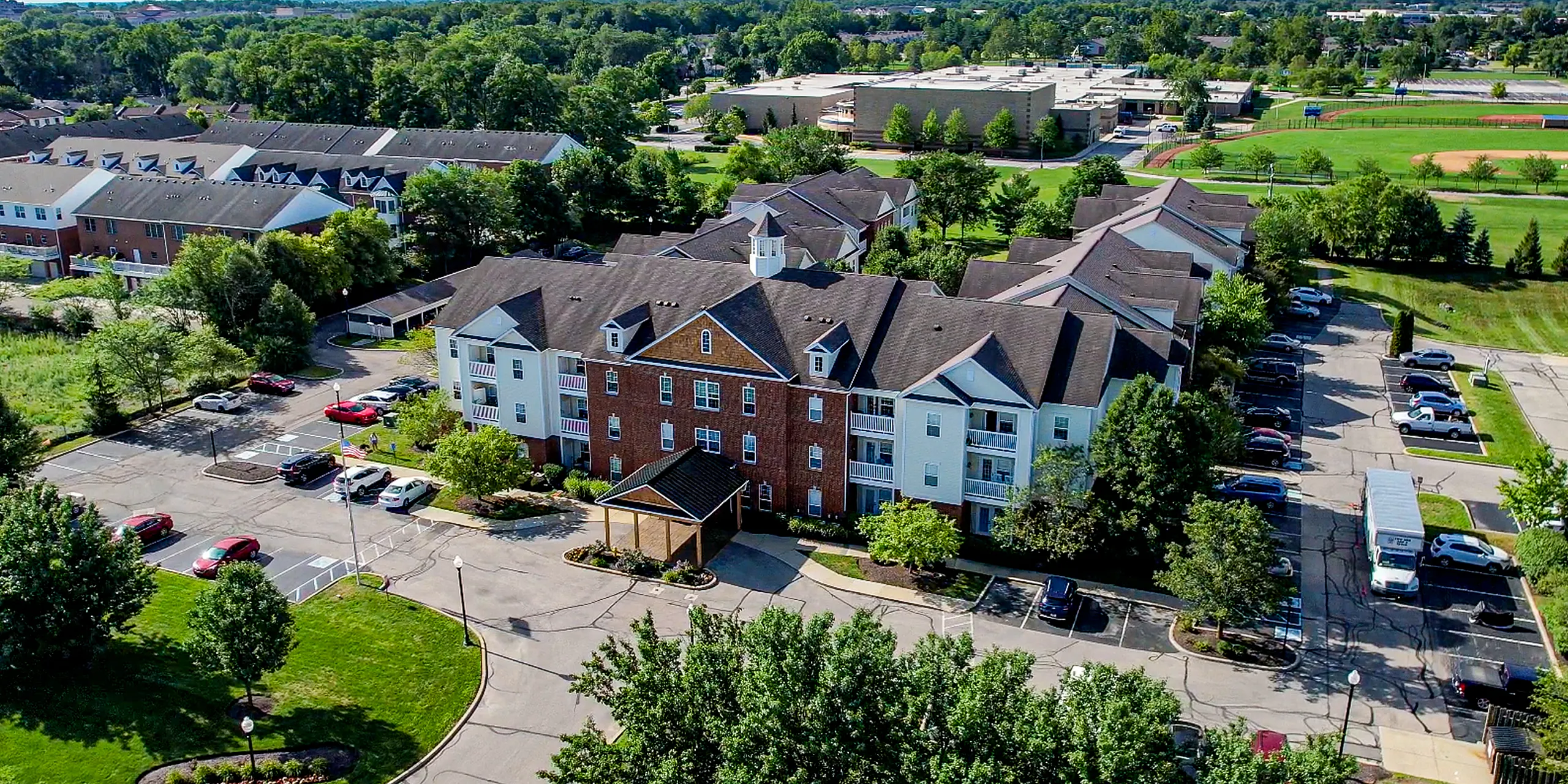 Charming apartment complex with a red-brick facade, surrounded by lush greenery and ample parking, located in a vibrant community.