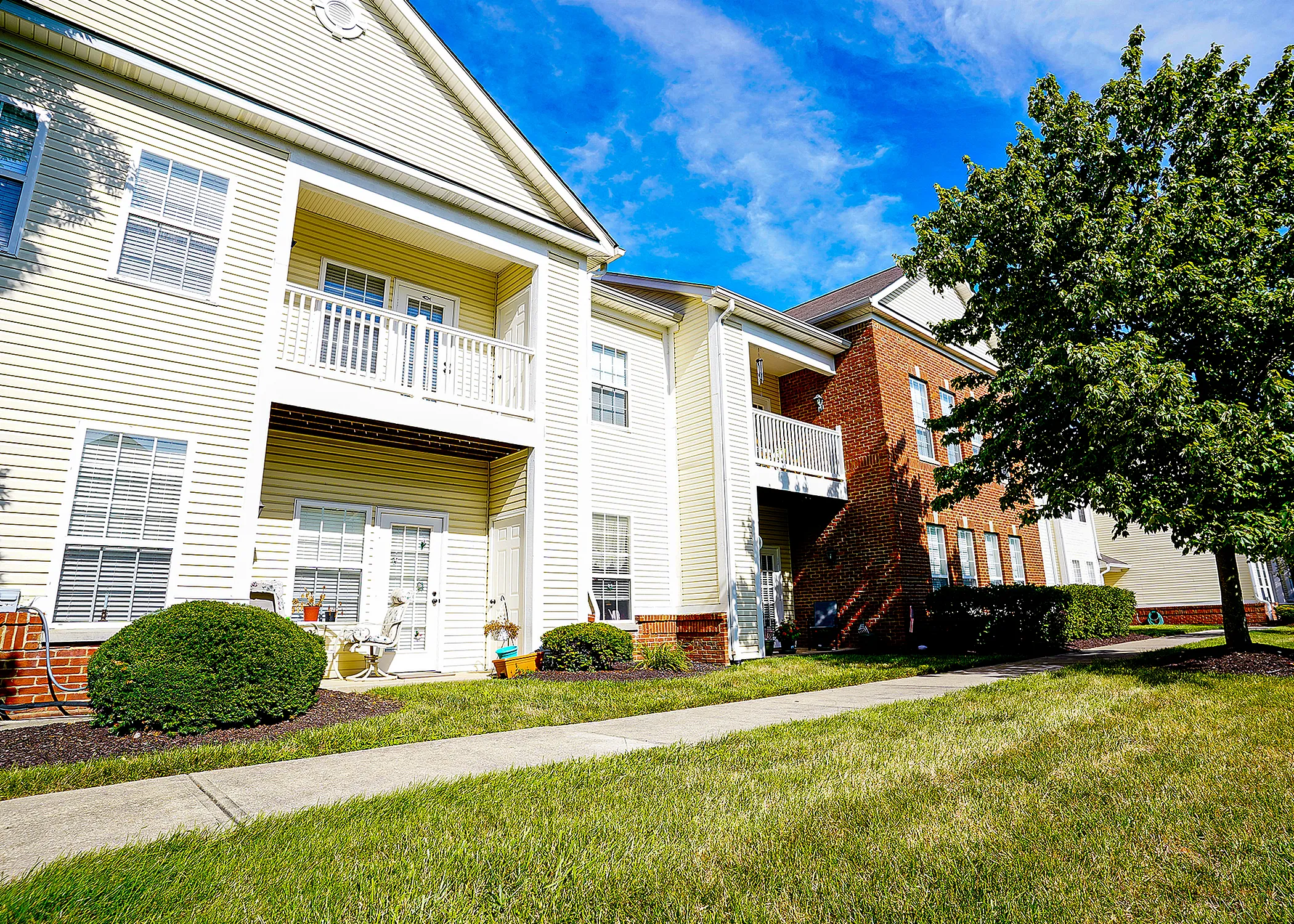 Charming apartment building with sunlit balconies, vibrant trees, and well-maintained gardens, showcasing comfortable and inviting living spaces.