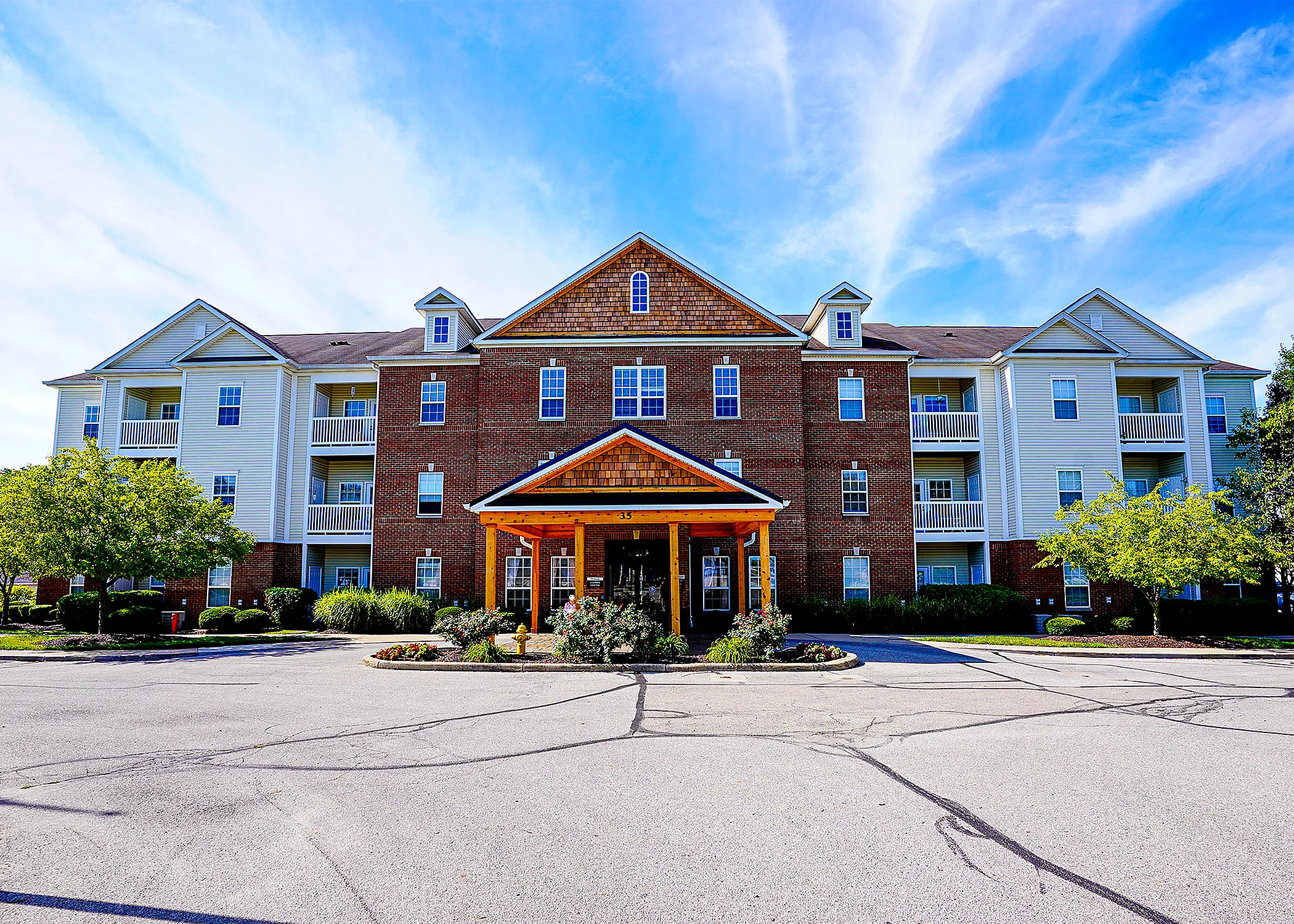 Charming multi-story apartment building with a welcoming entrance, surrounded by lush greenery and vibrant landscaping under a clear blue sky.