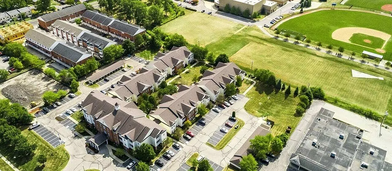 Aerial view of a charming apartment complex surrounded by lush greenery, showcasing convenient parking, and sports fields nearby.