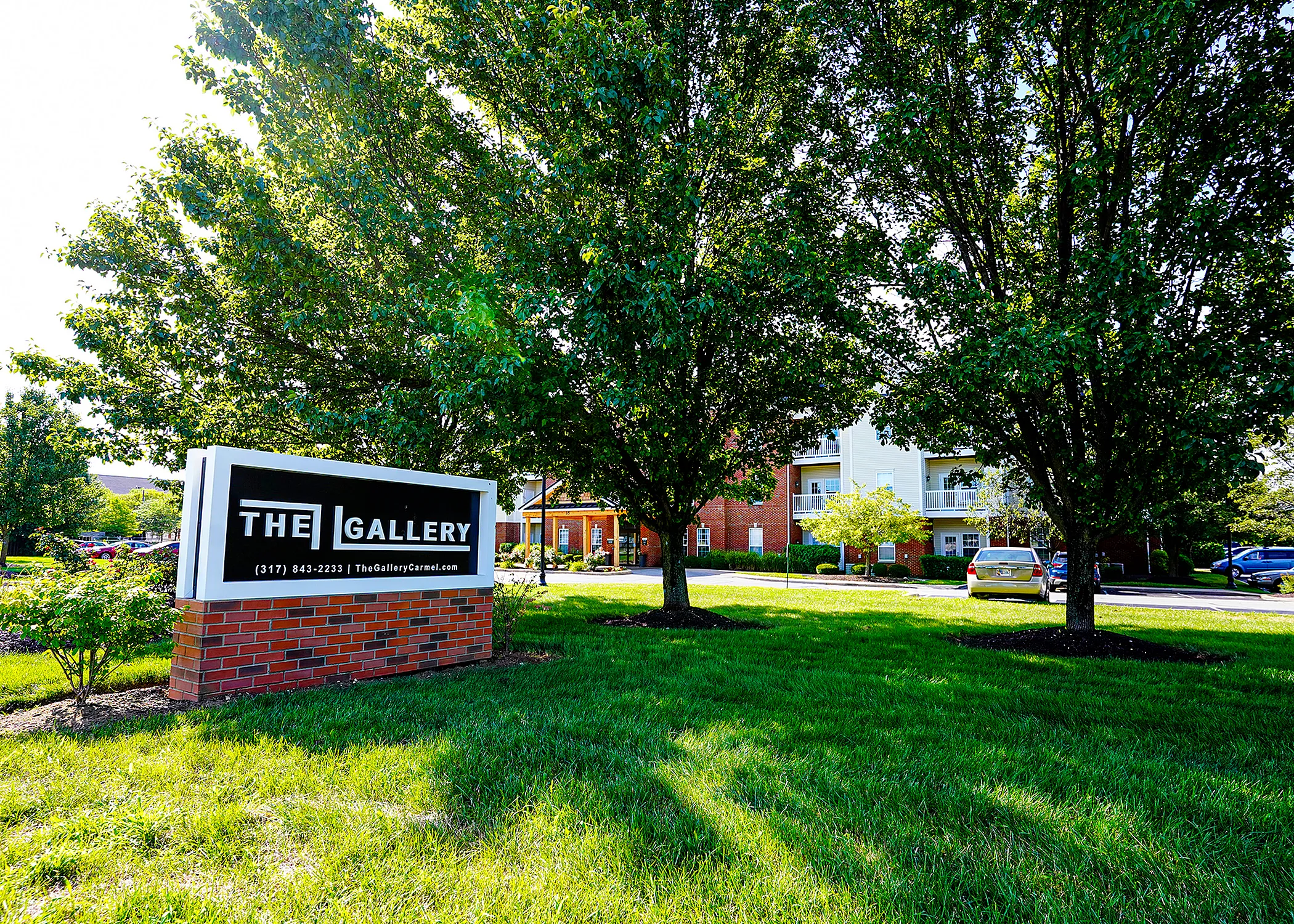 Inviting apartment complex entrance with lush greenery and modern signage at The Gallery in a serene setting.