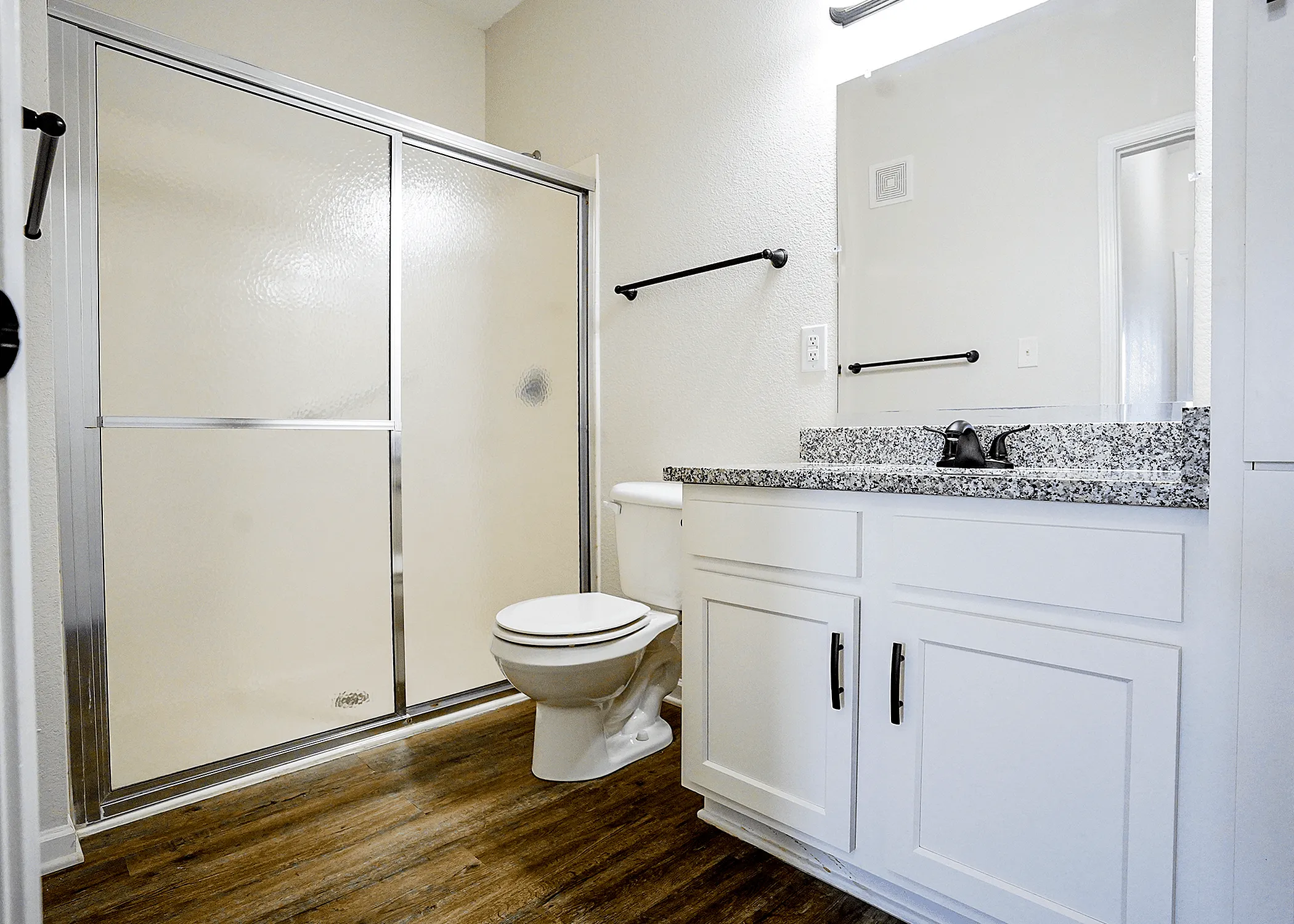 Modern bathroom featuring elegant granite countertops, sleek cabinetry, and a spacious glass-enclosed shower.