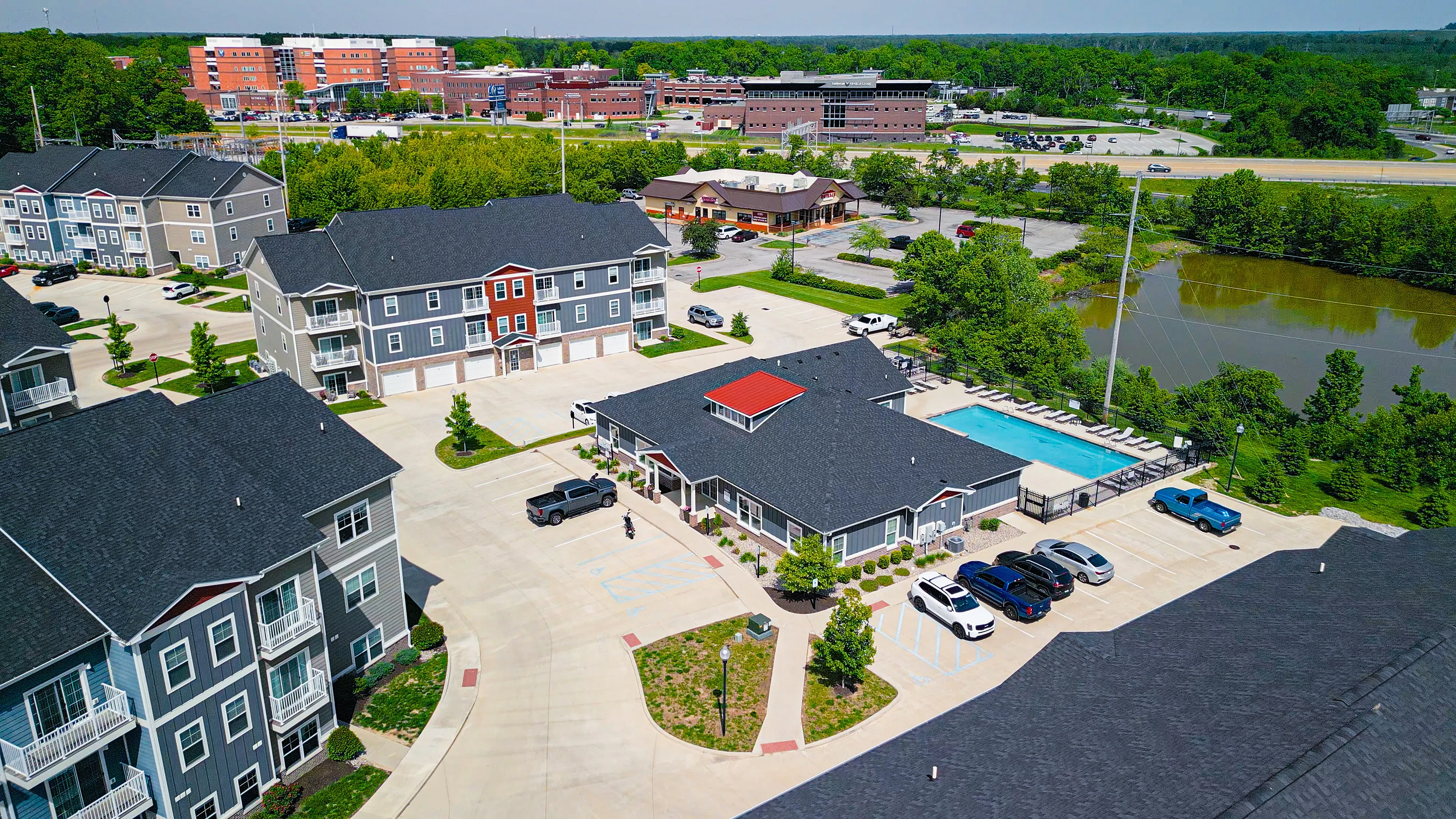 Vibrant aerial view of a modern apartment complex with a swimming pool, surrounded by lush greenery and ample parking space.
