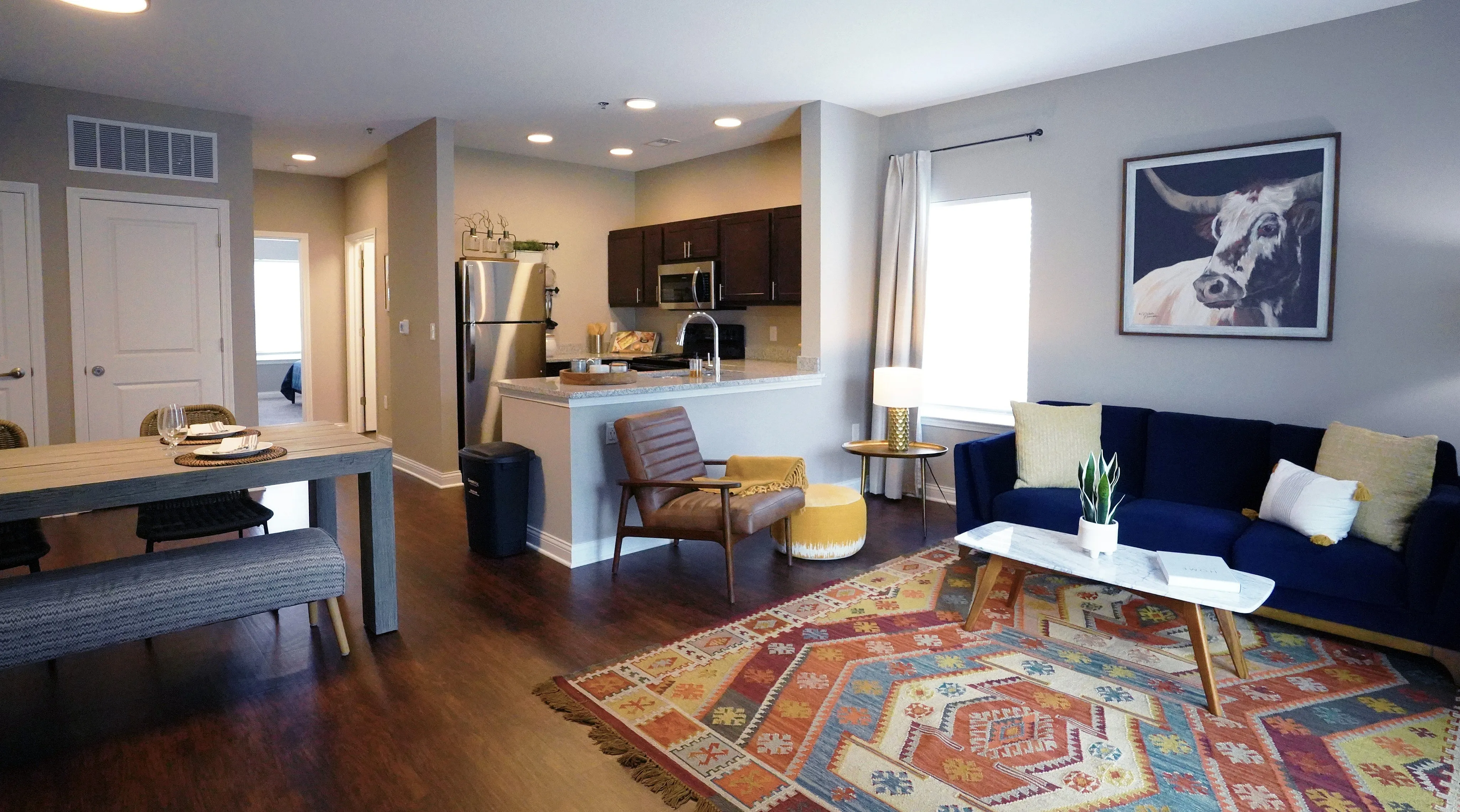 Chic open-concept living and dining area featuring a modern kitchen with stainless steel appliances, vibrant artwork, and cozy seating on a colorful patterned rug.