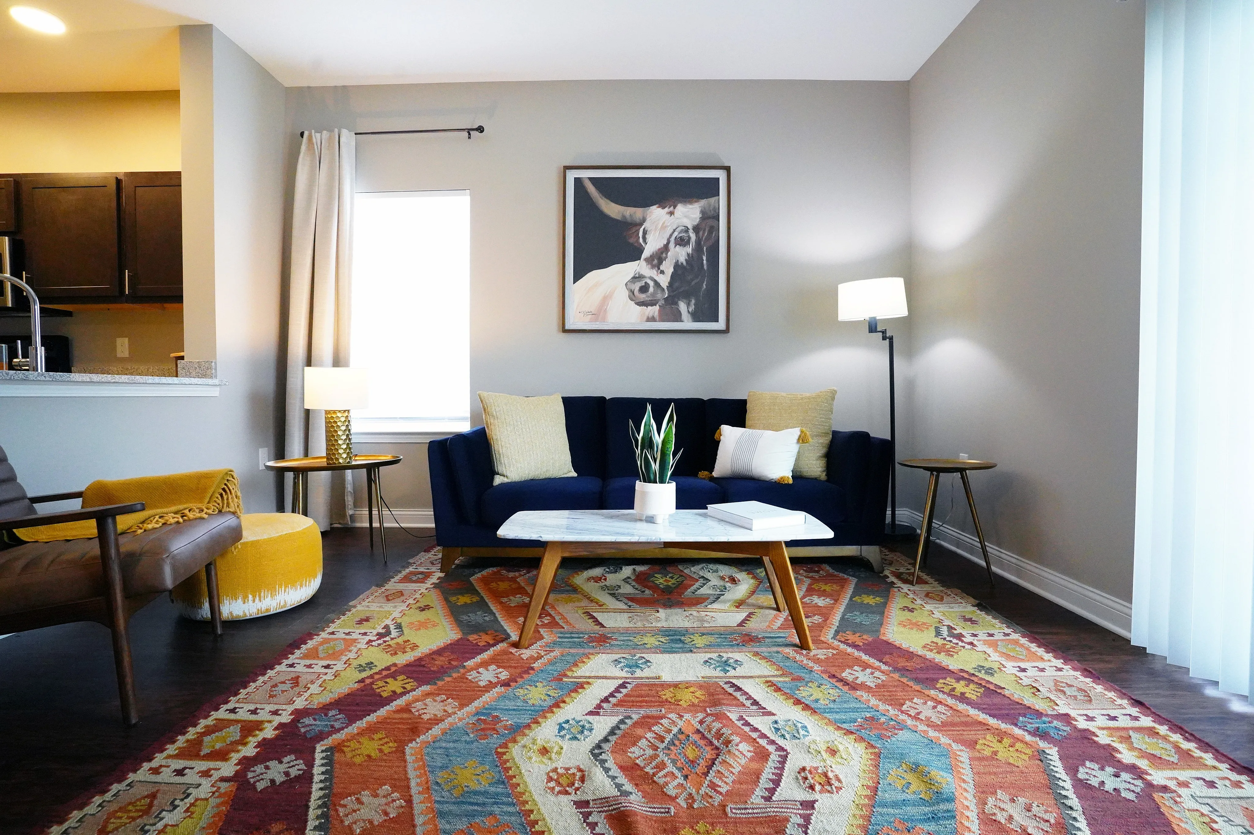 Chic living room with a vibrant geometric-patterned rug, stylish navy sofa, and modern armchair. An elegant plant adorns the sleek coffee table, with sophisticated lighting creating a cozy ambiance.