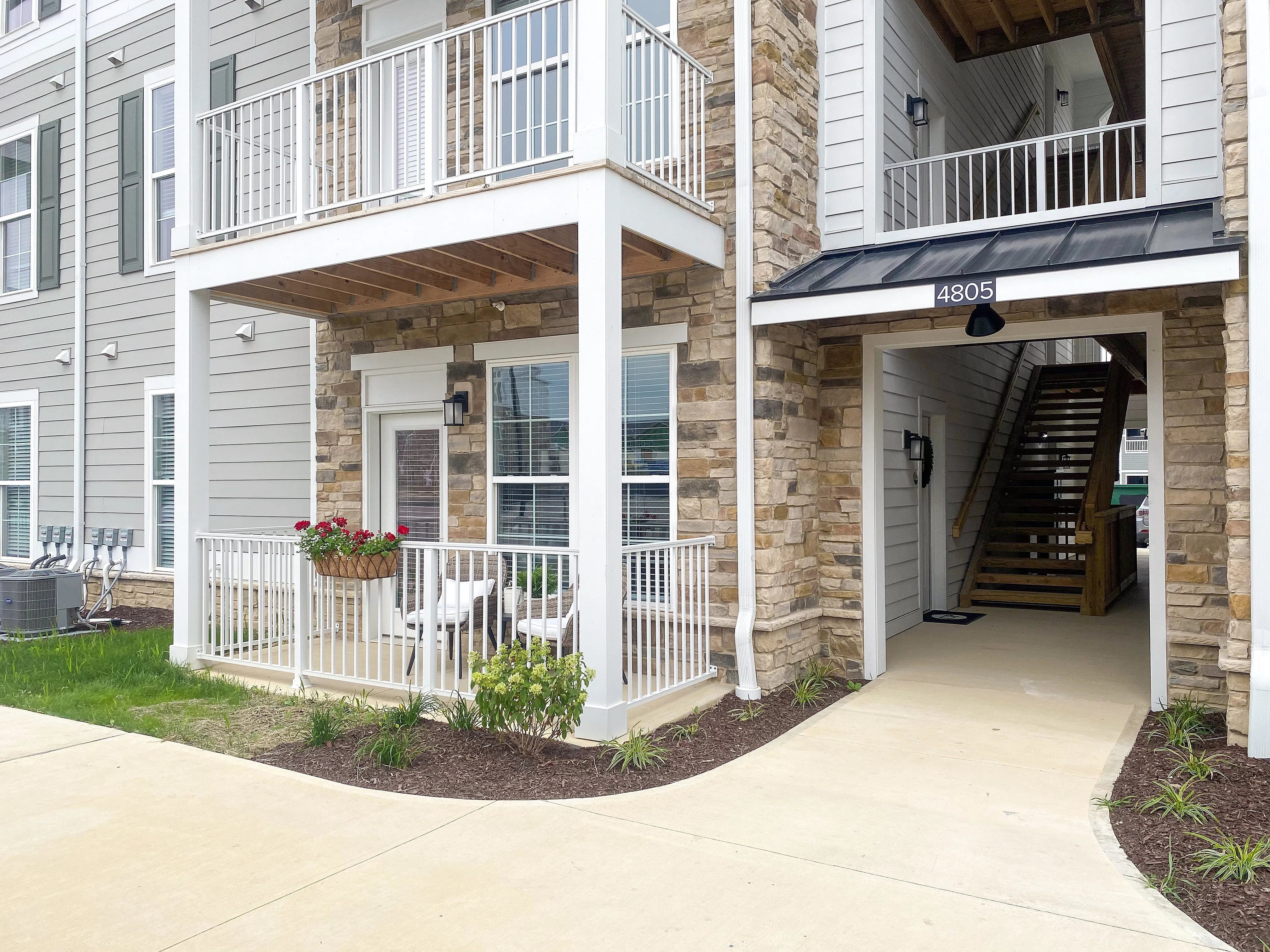 Charming apartment exterior with stone and siding finish, featuring a cozy balcony adorned with vibrant flowers and inviting entryway.