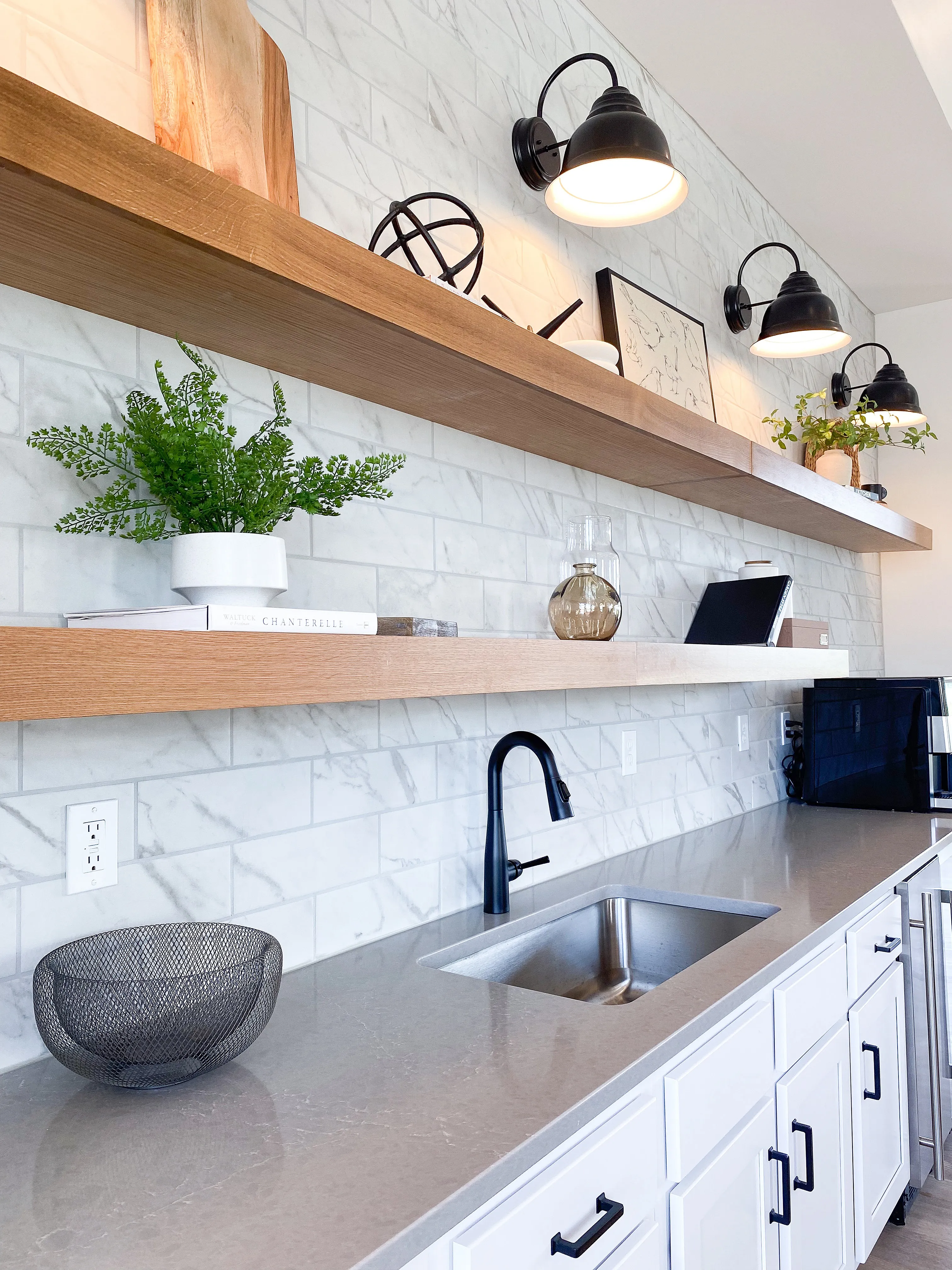 Modern kitchen with sleek white cabinets, elegant marble backsplash, and open wooden shelves accented with plants and decor.