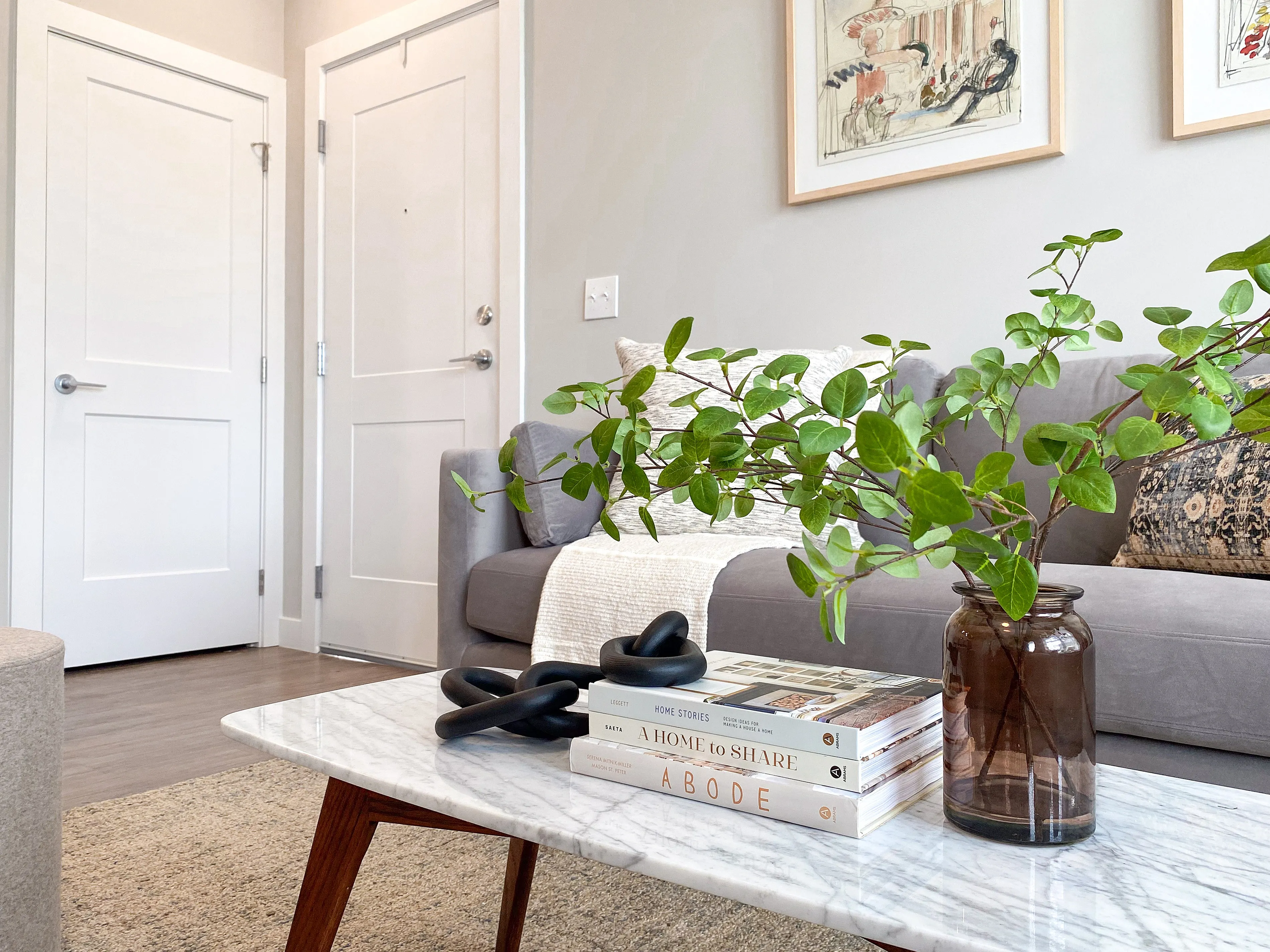 Chic and cozy living room with a plush gray sofa, stylish marble coffee table with decor and books, and vibrant green plant inviting warmth and elegance.