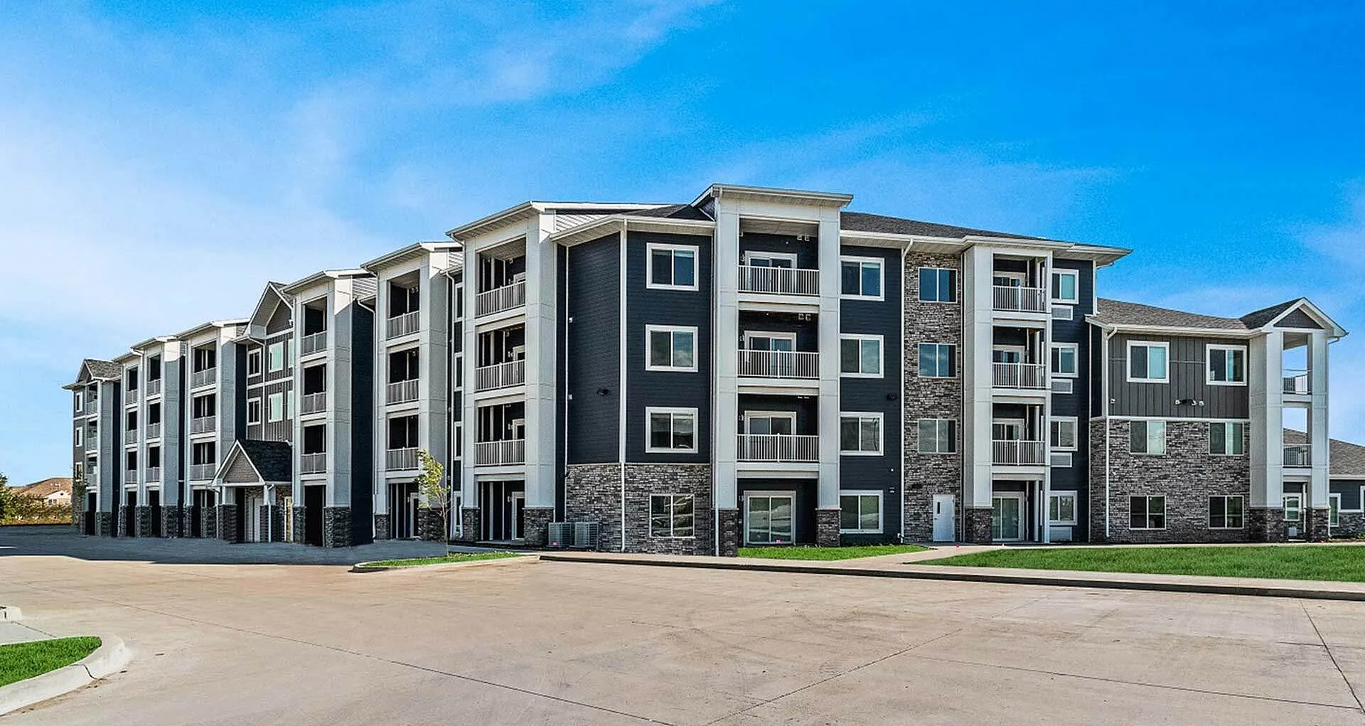 Modern, multi-story apartment building with elegant facade, spacious balconies, and landscaped surroundings under a clear blue sky.