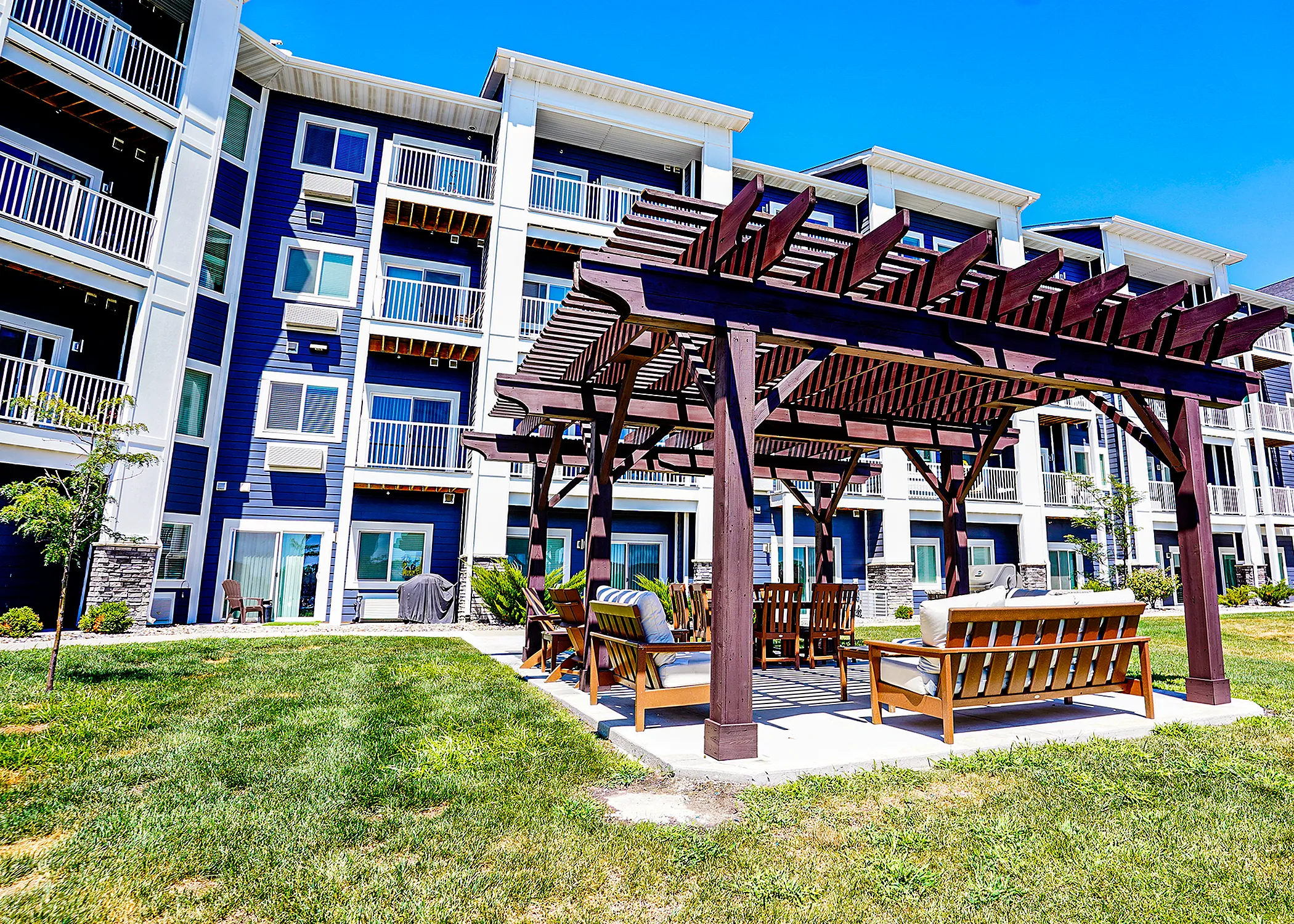 Charming apartment building with modern balconies and inviting outdoor pergola seating area, perfect for relaxing under clear blue skies.