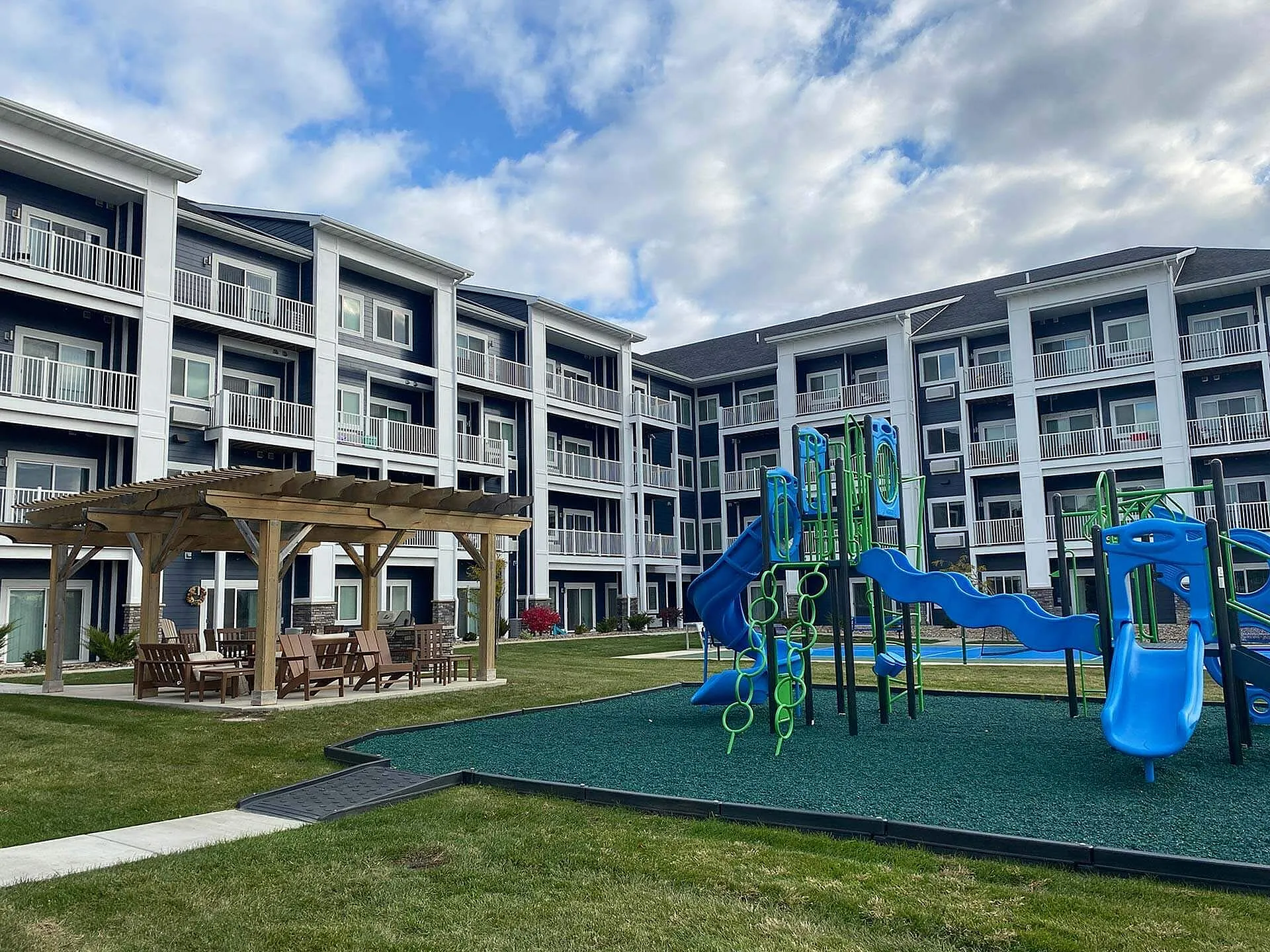 Modern apartment complex with inviting balconies, a vibrant playground, and a charming outdoor seating area under a pergola.