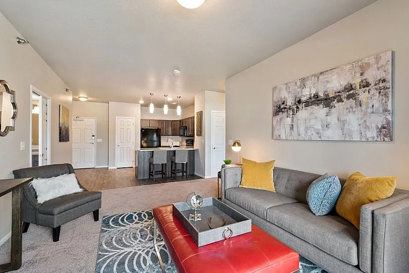 Contemporary open-concept living room with stylish decor, featuring a plush gray sofa, vibrant accent pillows, chic wall art, and a modern kitchen in the background.
