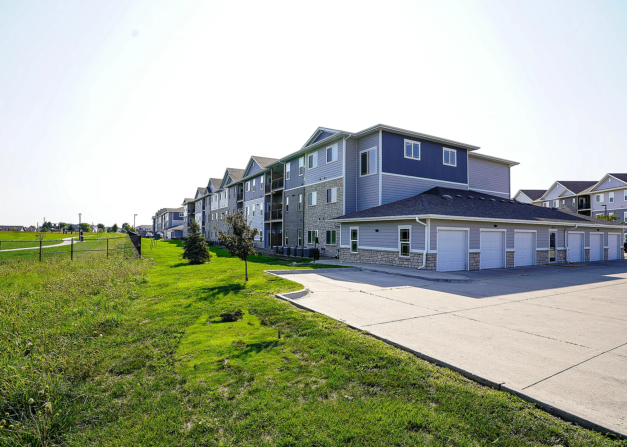 Modern apartment complex with elegant architecture, featuring individual garages and lush green surroundings under a clear sky.